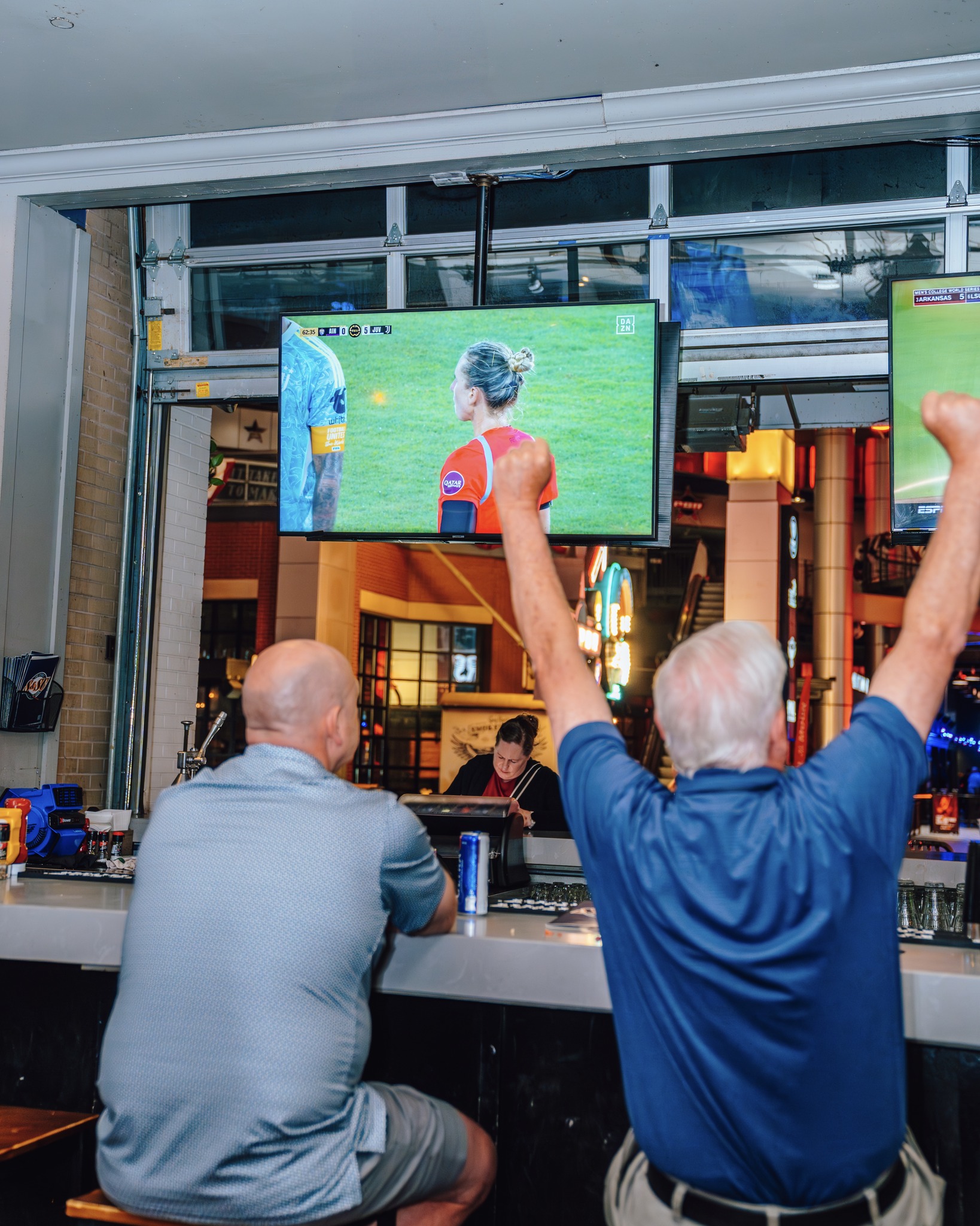 An image of two fans watching soccer at the bar and cheering.