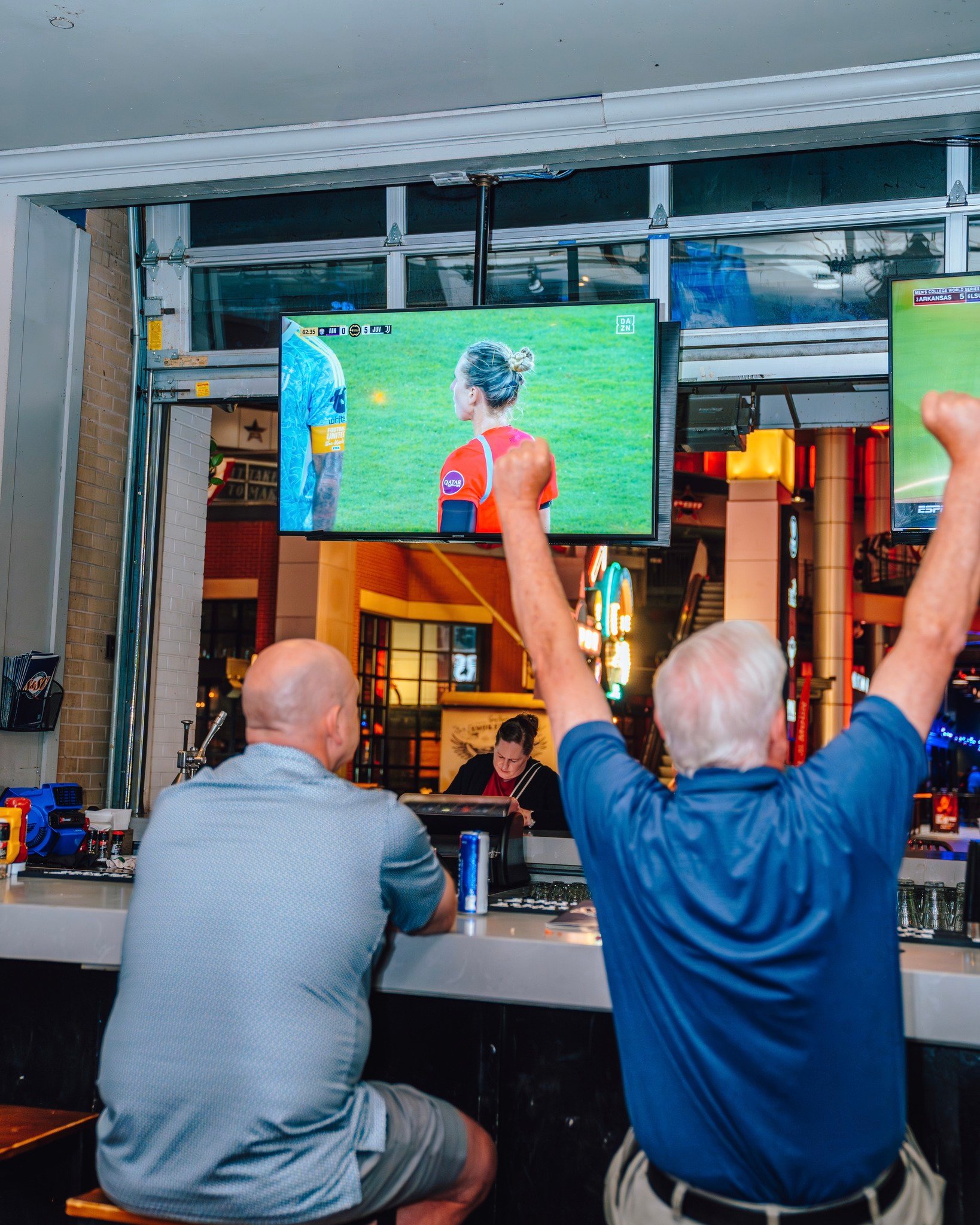 An image of two fans watching soccer at the bar and cheering.