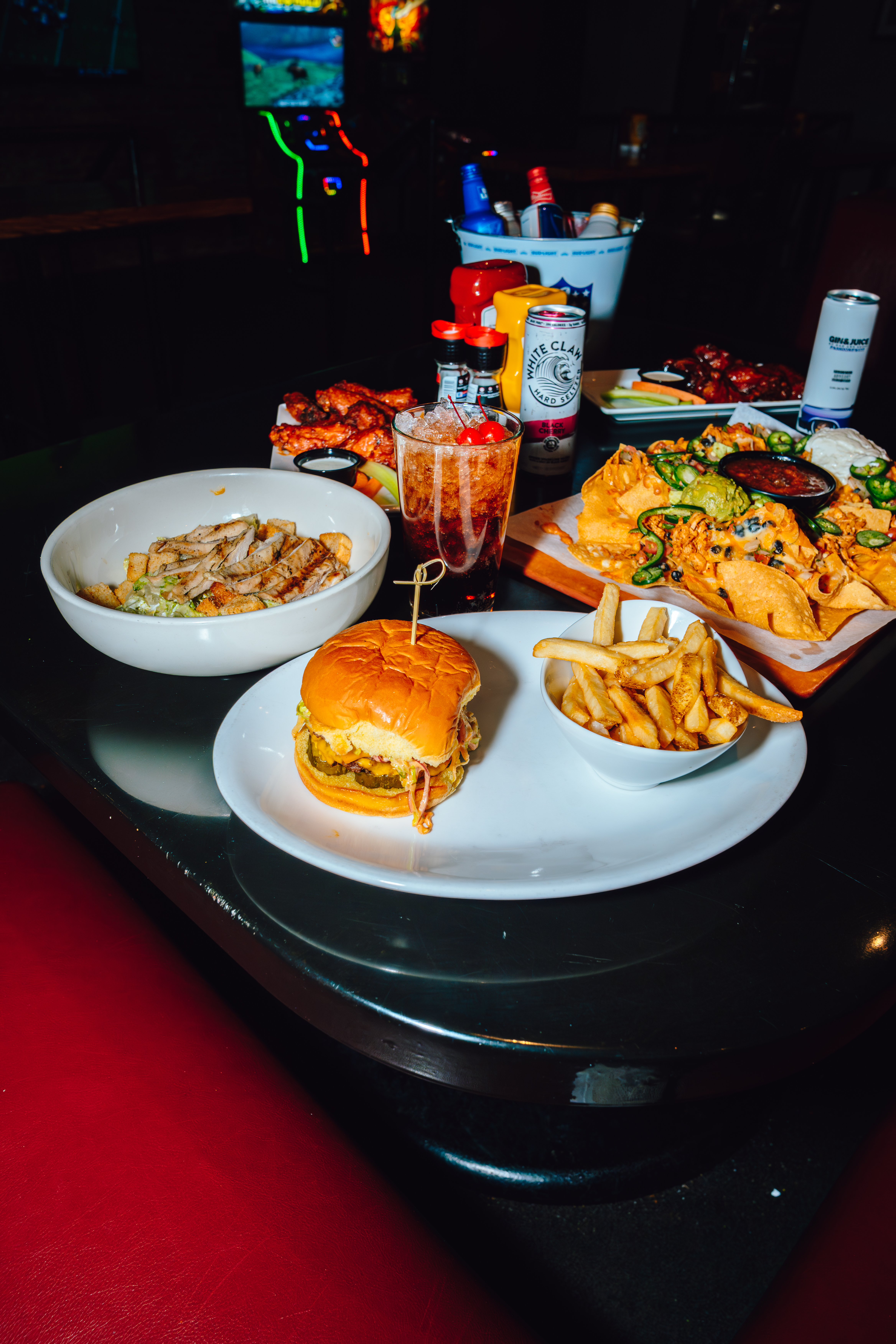 An image of a table filled with food at Sports and Social that includes a burger, loaded nachos, and more.