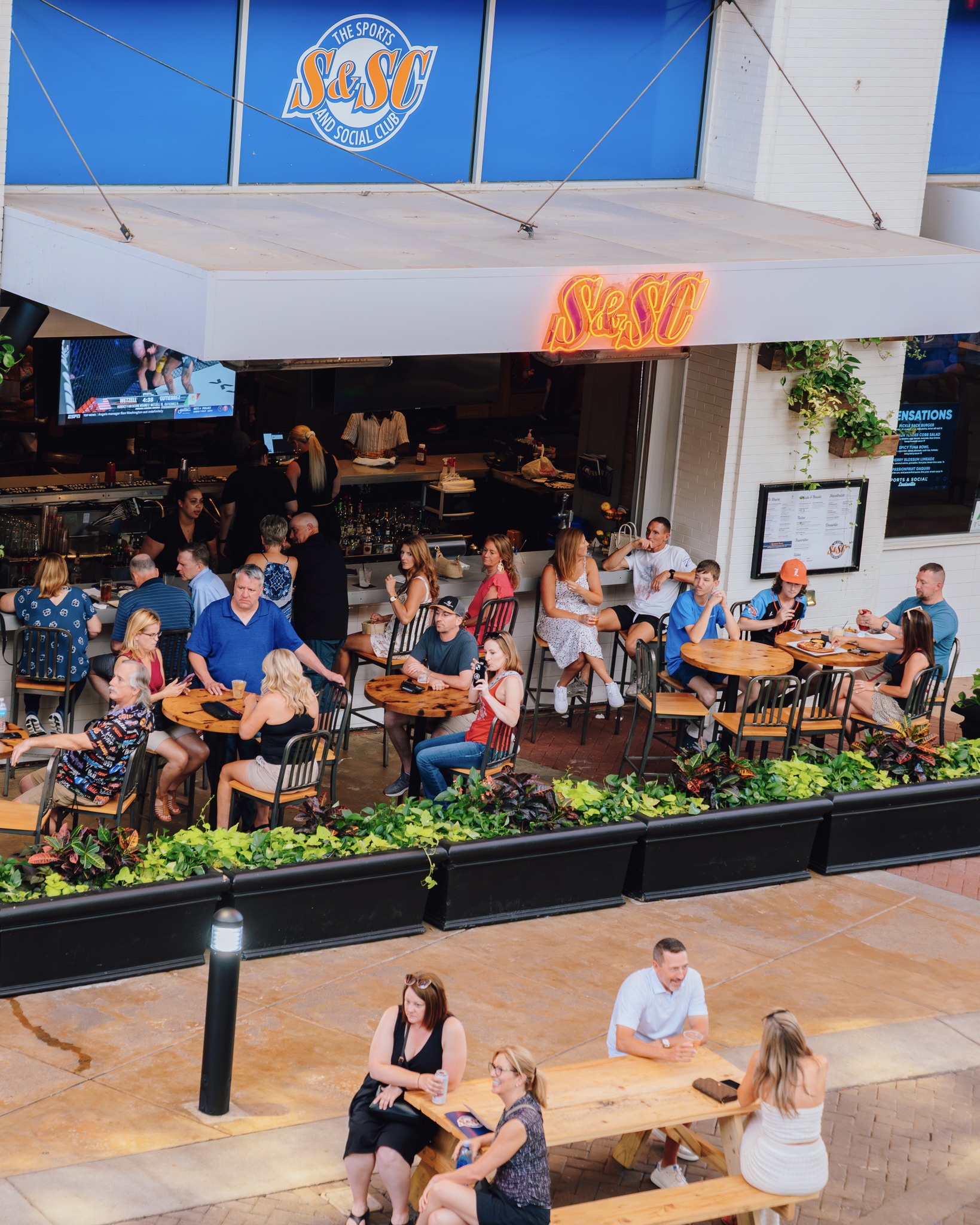 A wide view shot of the entire Sports and Social patio filled with people sitting at tables.