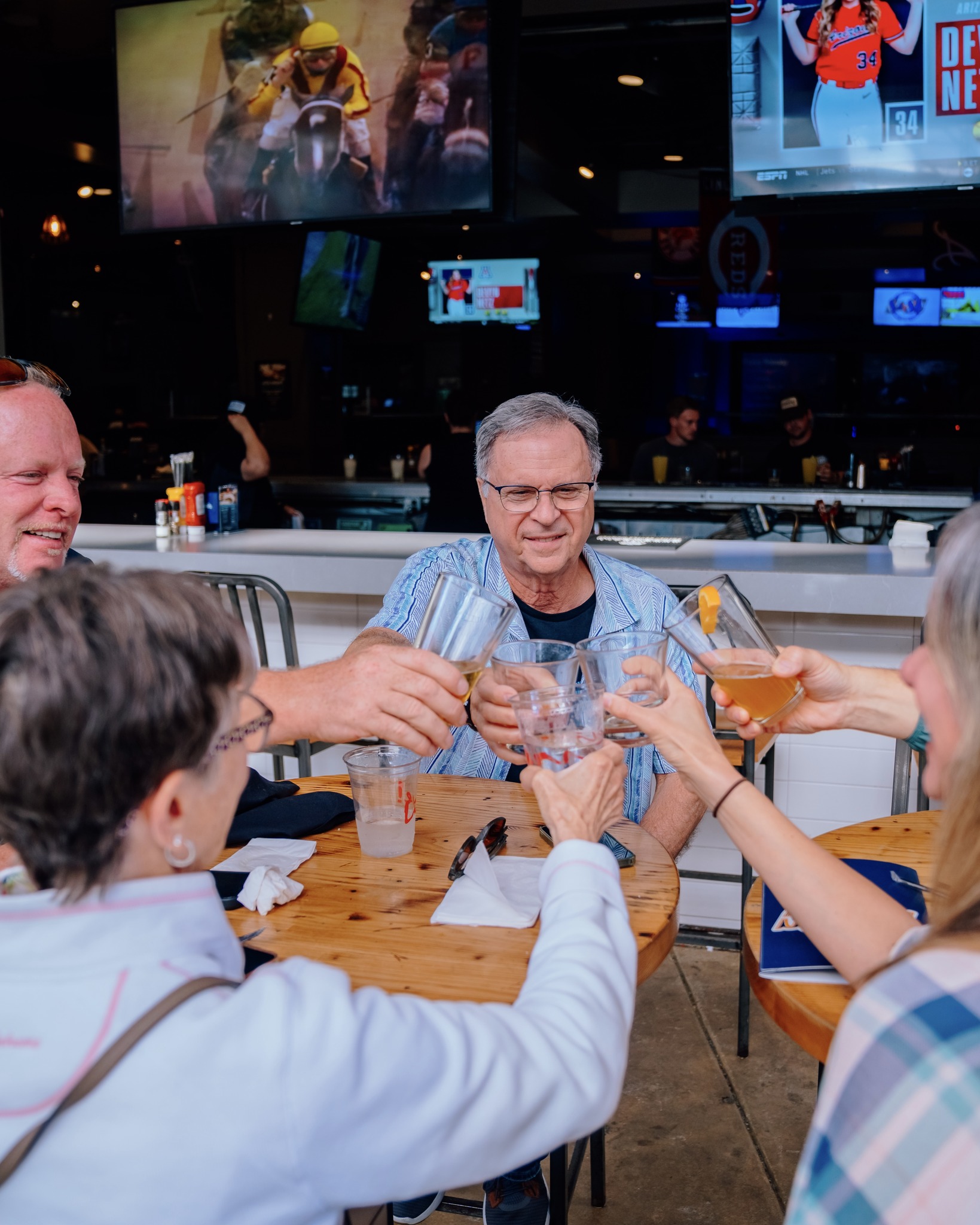 An image of people sitting on the patio outside of Sports and Social and cheering their drinks.