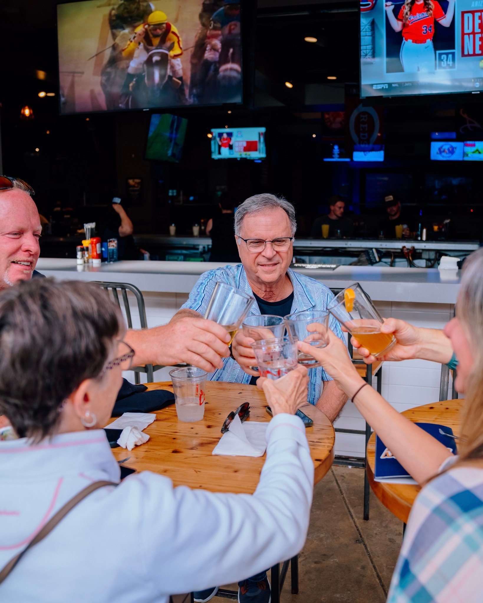 An image of people sitting on the patio outside of Sports and Social and cheering their drinks.