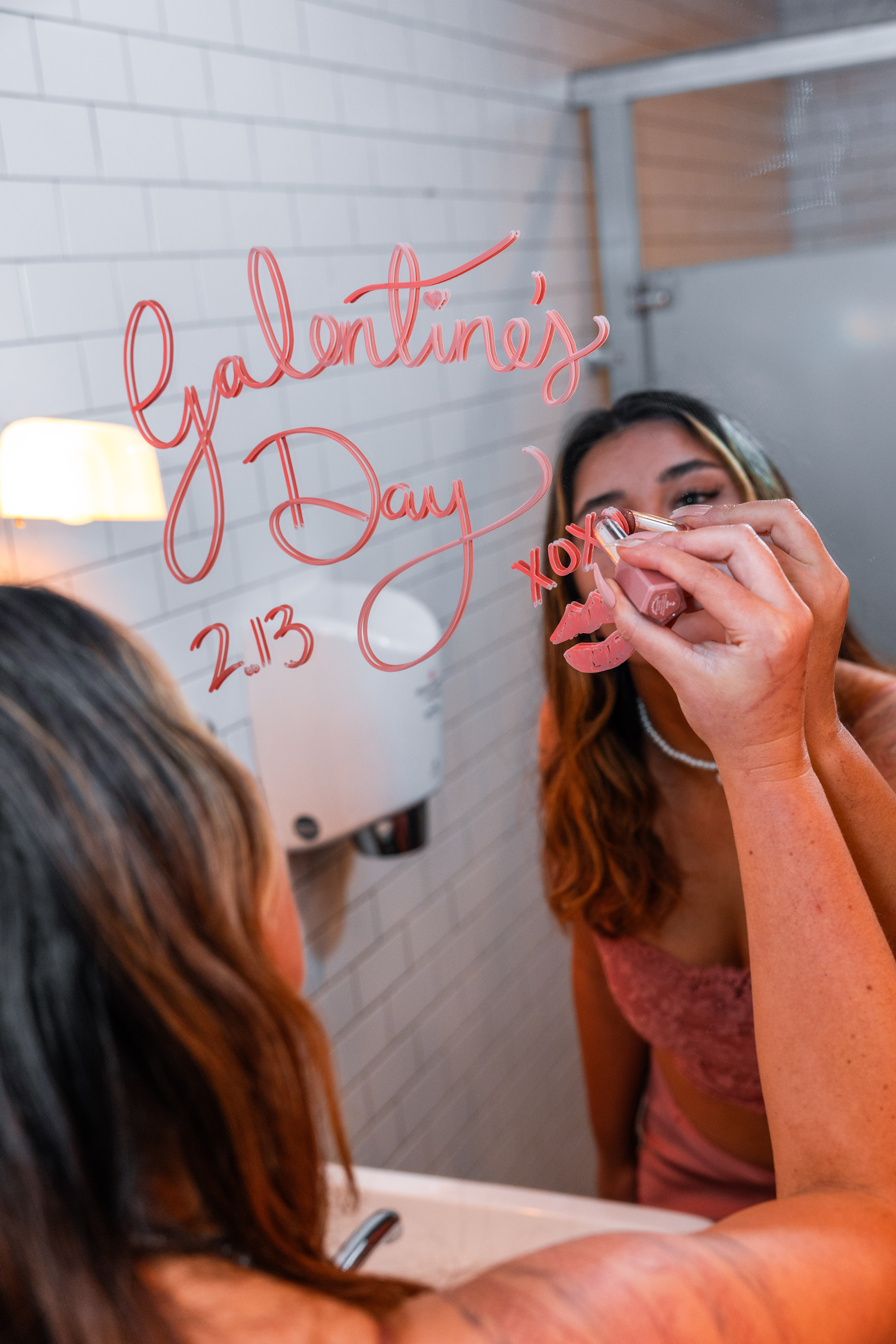 Girl writing "Galentine's Day" on mirror with Lipstick
