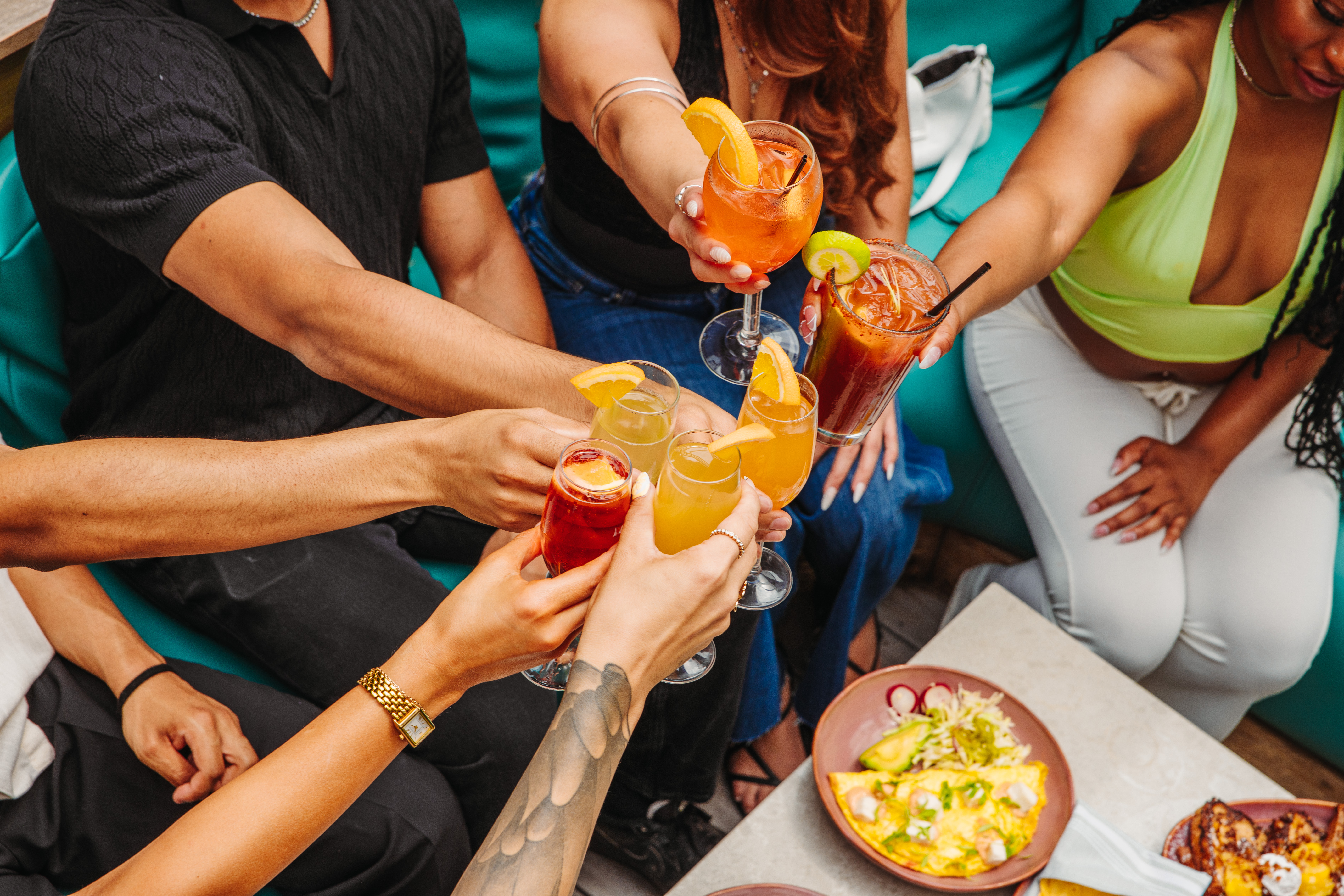 A group of friends on the Besos patio holding vibrant brunch cocktails.