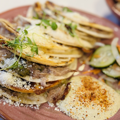 Stack of beef tacos garnished with cheese, onions and greens on a mauve-colored plate.