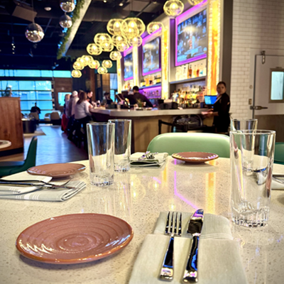 Fully set dining table at Besos y Abrazos with bar in the backround.