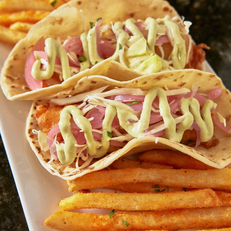 Two fish tacos with French fries on white plate.