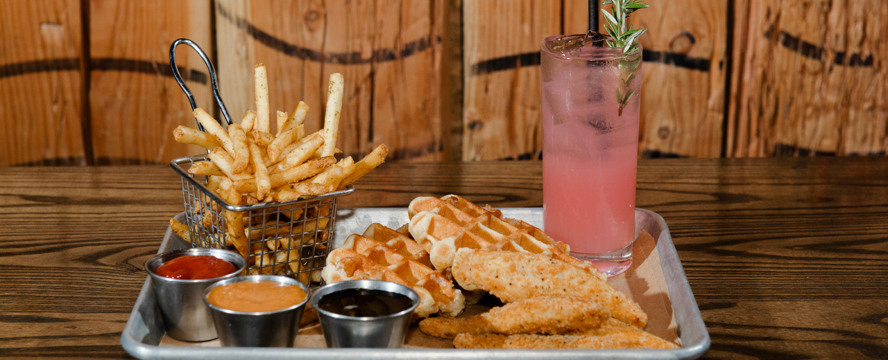 Tray of food with waffles, fries, and a cocktail