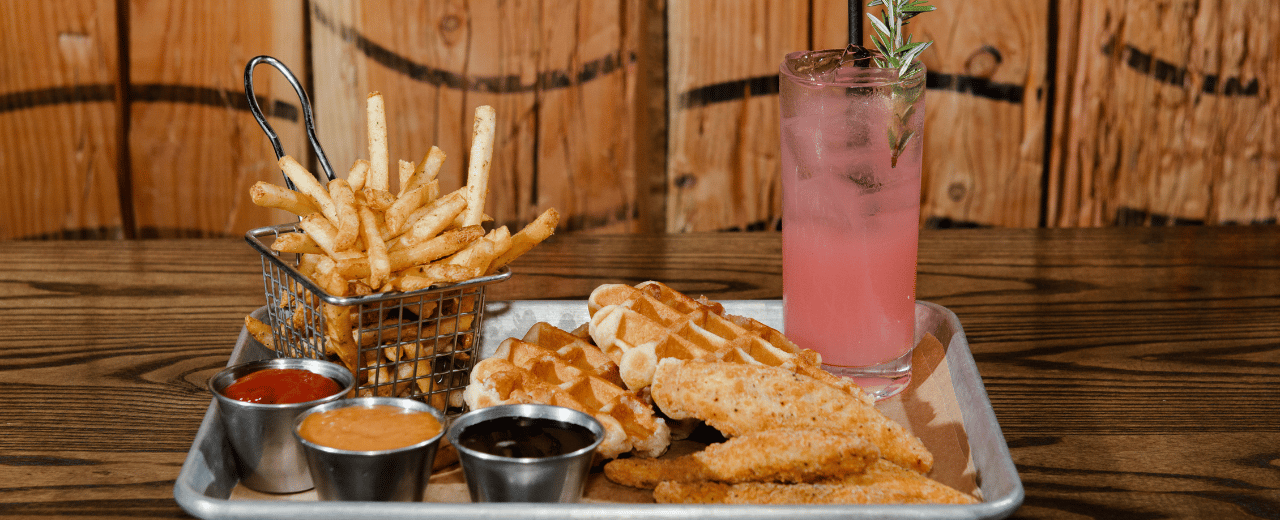 Tray of food with waffles, fries, and a cocktail