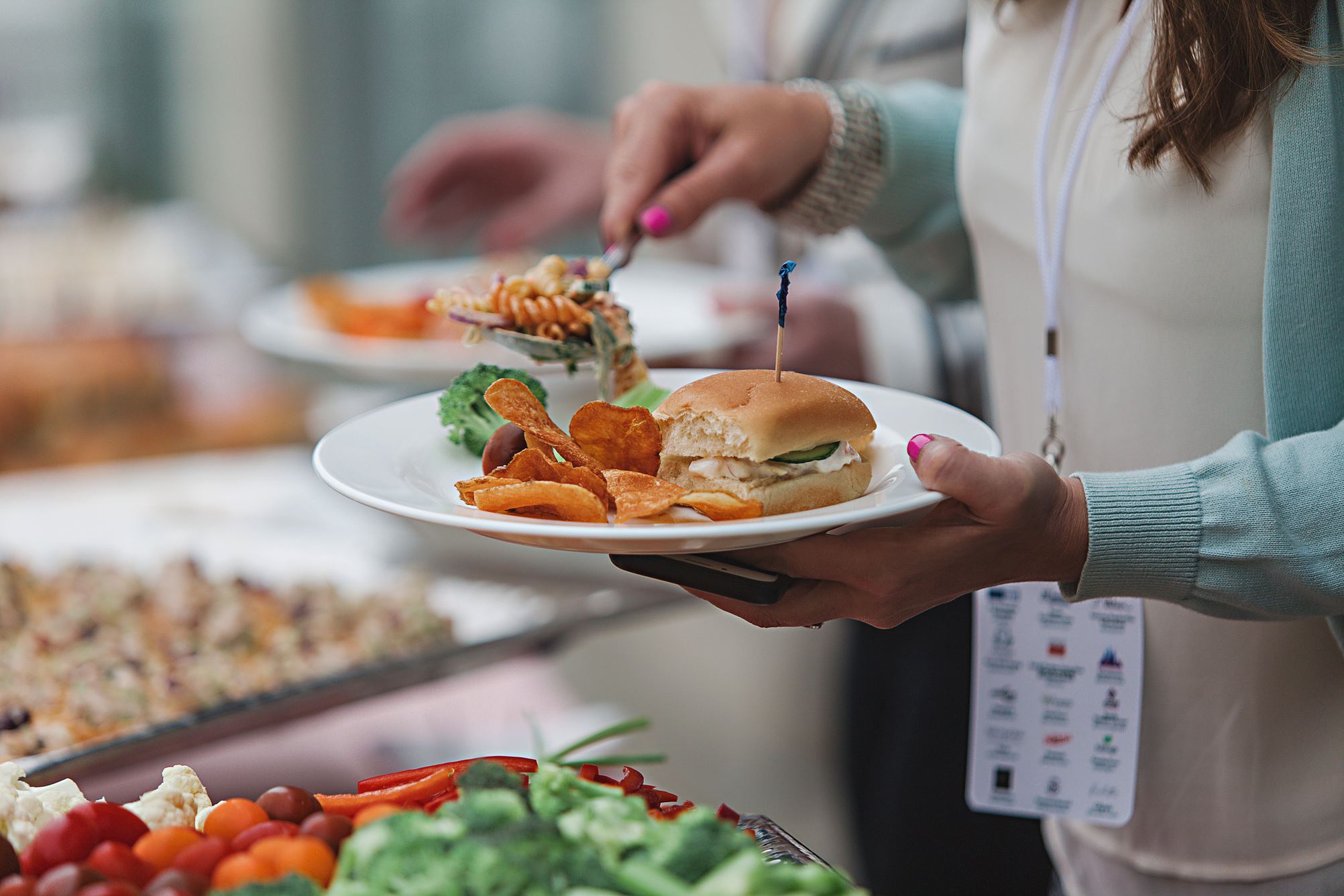 People standing at a catering table placing food on their plate. 