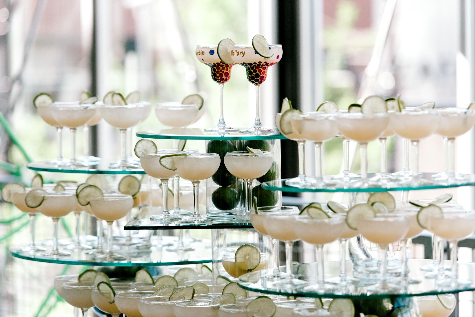 Several pretty cocktails sitting on glass tables, arranged into an impressive tower.