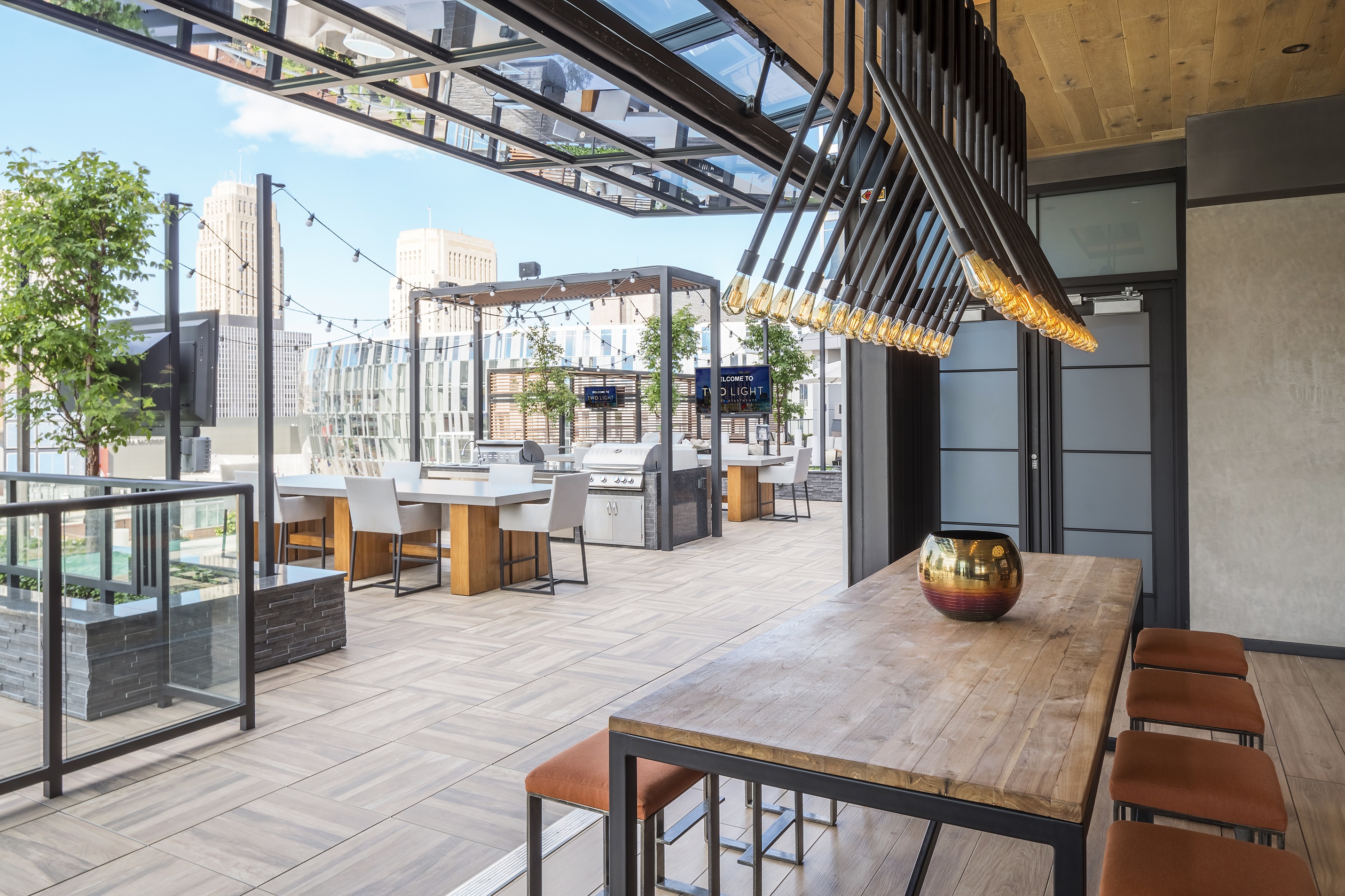 Partially covered deck with TV viewing area, high-end grills, and table seating at Two Light luxury apartment building.