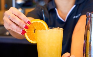 Close up photo of a Sports & Social waitress putting an orange slice on an orange crush cocktail.