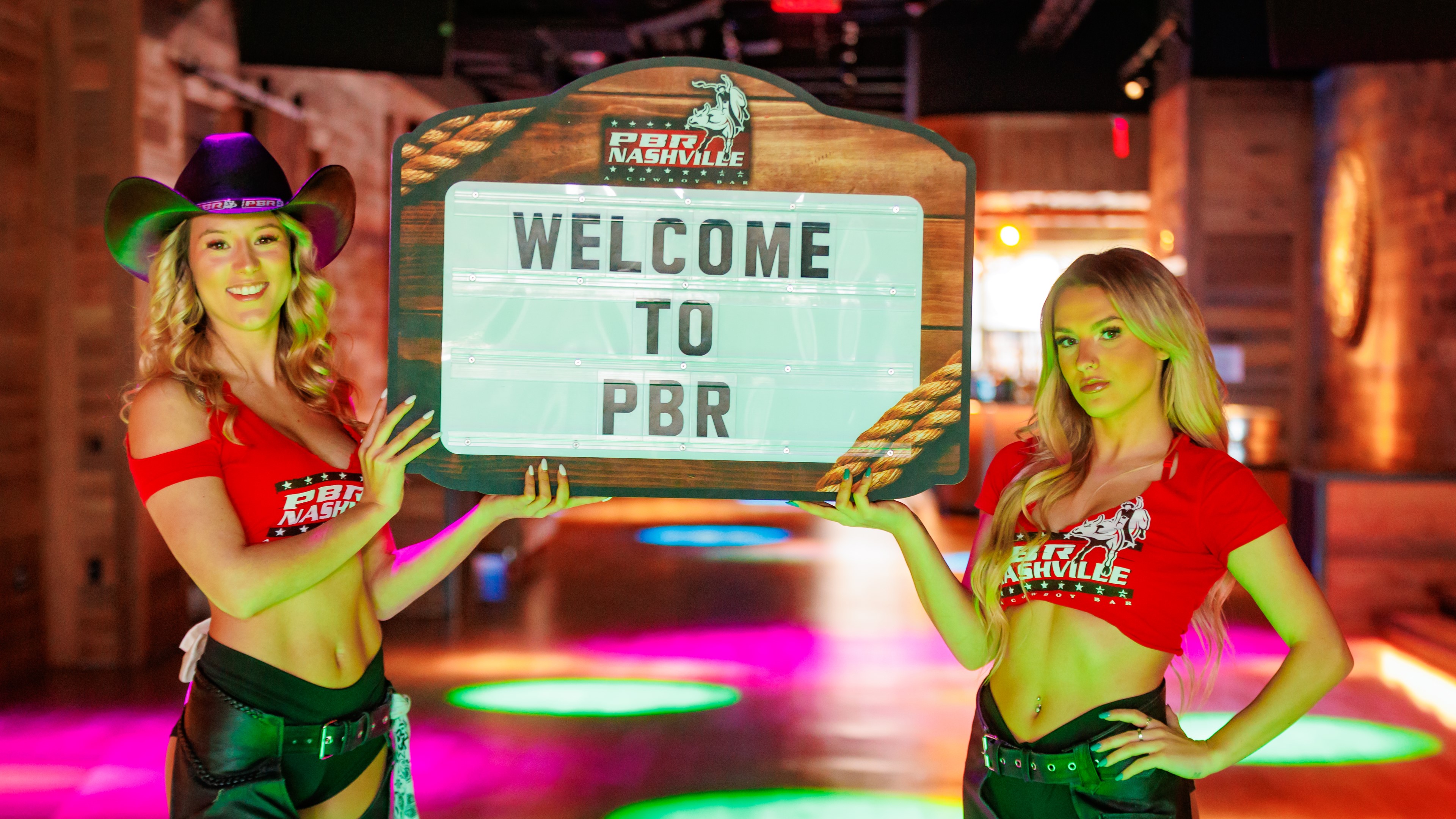 Two buckle bunnies holding either side of a 'Welcome to PBR' sign.