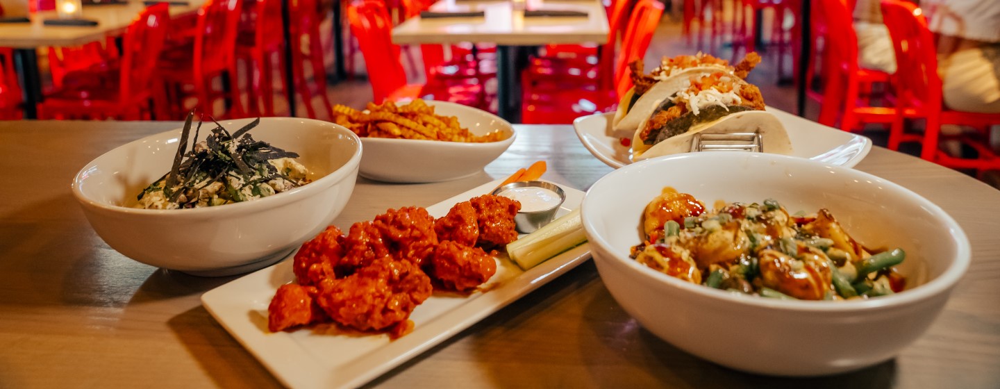 Crinkle french fries, saucy chicken wings and ranch, and crispy ancho-spiced chicken soft and crunchy taco on white plates wrap at Sports & Social at Live! at the Pointe Orlando.