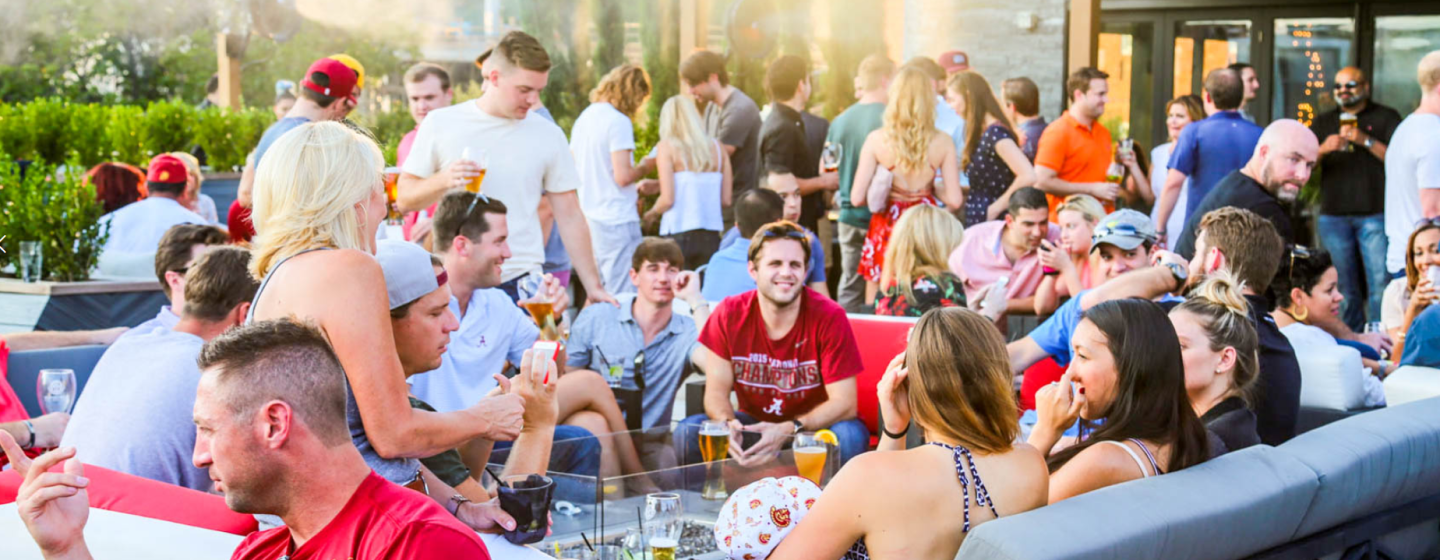 Guests standing and sitting on couches at a daytime outdoor event at Sports & Social.