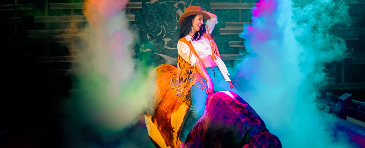 Woman riding the mechanical bull at PBR Cowboy Bar at Live! at the Pointe Orlando.
