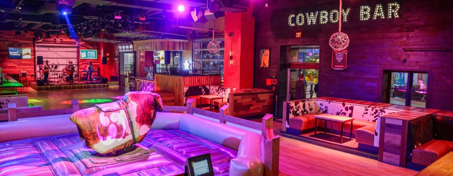 Wide shot of band on stage, mechanical bull, and booth seating at PBR Cowboy Bar at Live! at the Pointe Orlando.
