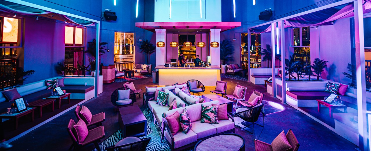 Palm Tree Club lounge seating and DJ booth at night with warm blue and pink lighting.