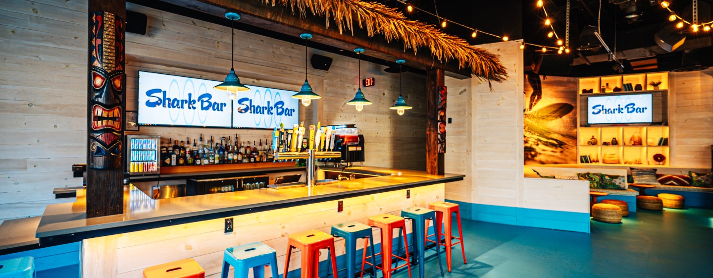 Main bar with tiki theme and teal and orange metal barstools at Shark Bar at Live! at the Pointe Orlando.