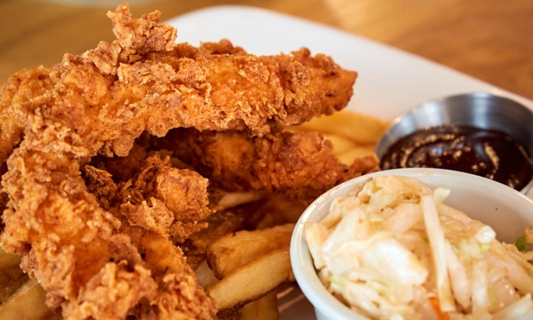 Chicken tenders, fries, side and sauce on white plate.