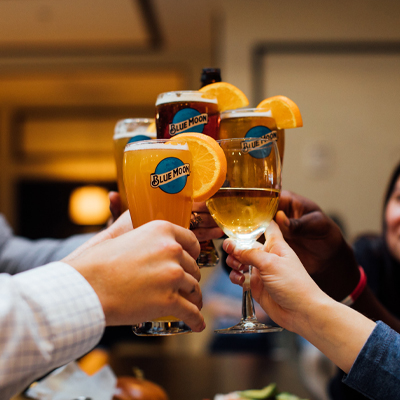 Pint glasses of Blue Moon beer with orange slice garnish being toasted.
