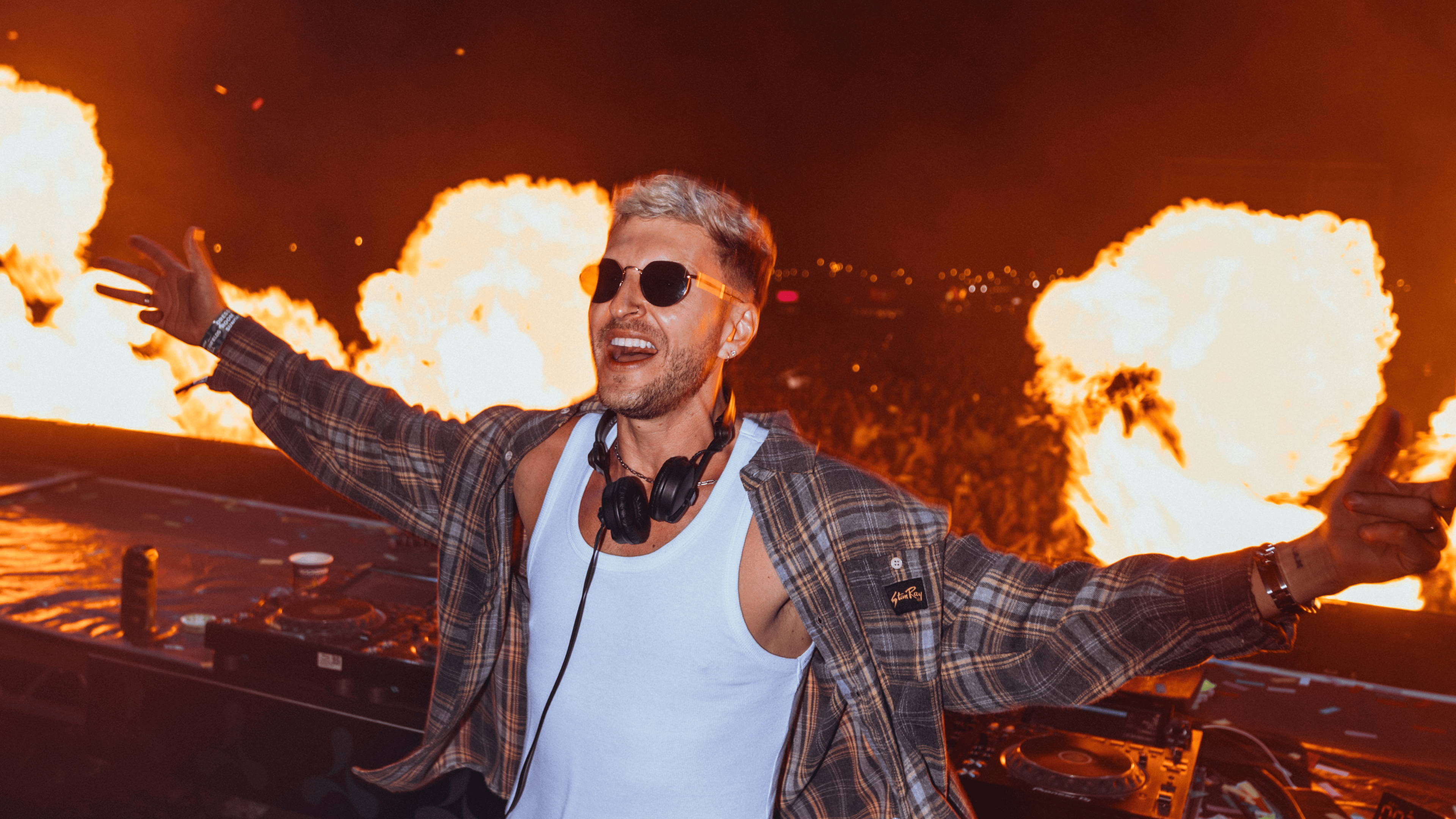 Image of a man, DOD, posing for a pic at his DJ set with a crowd behind him.