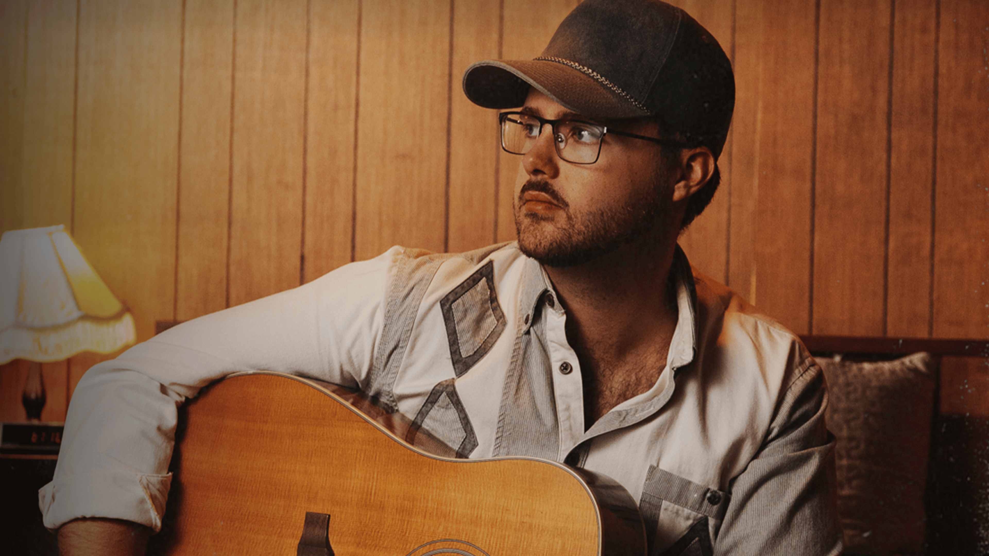 An image of a guy, Kenny Whitmore, sitting with his guitar.