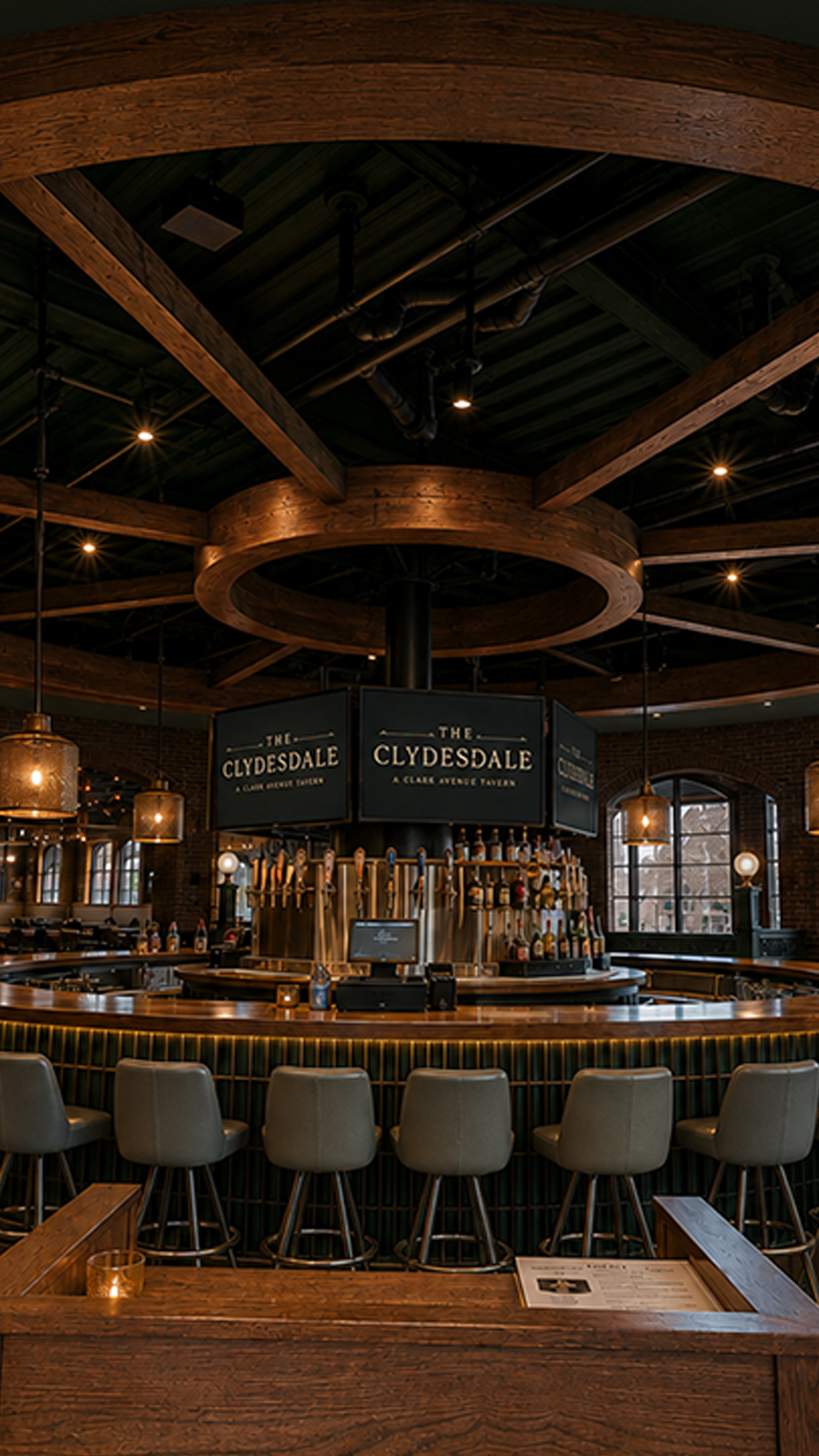 Circular bar in the center of The Clydesdale tavern featuring TVs, upolstered stools, and wood details.