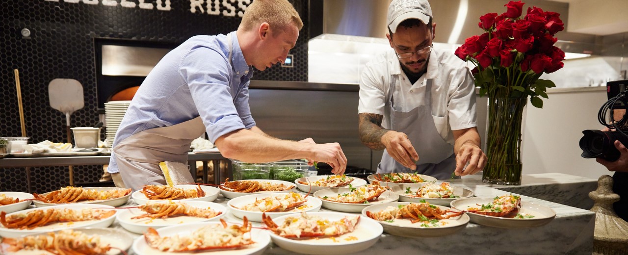 Two male chefs preparing several dinner plates.