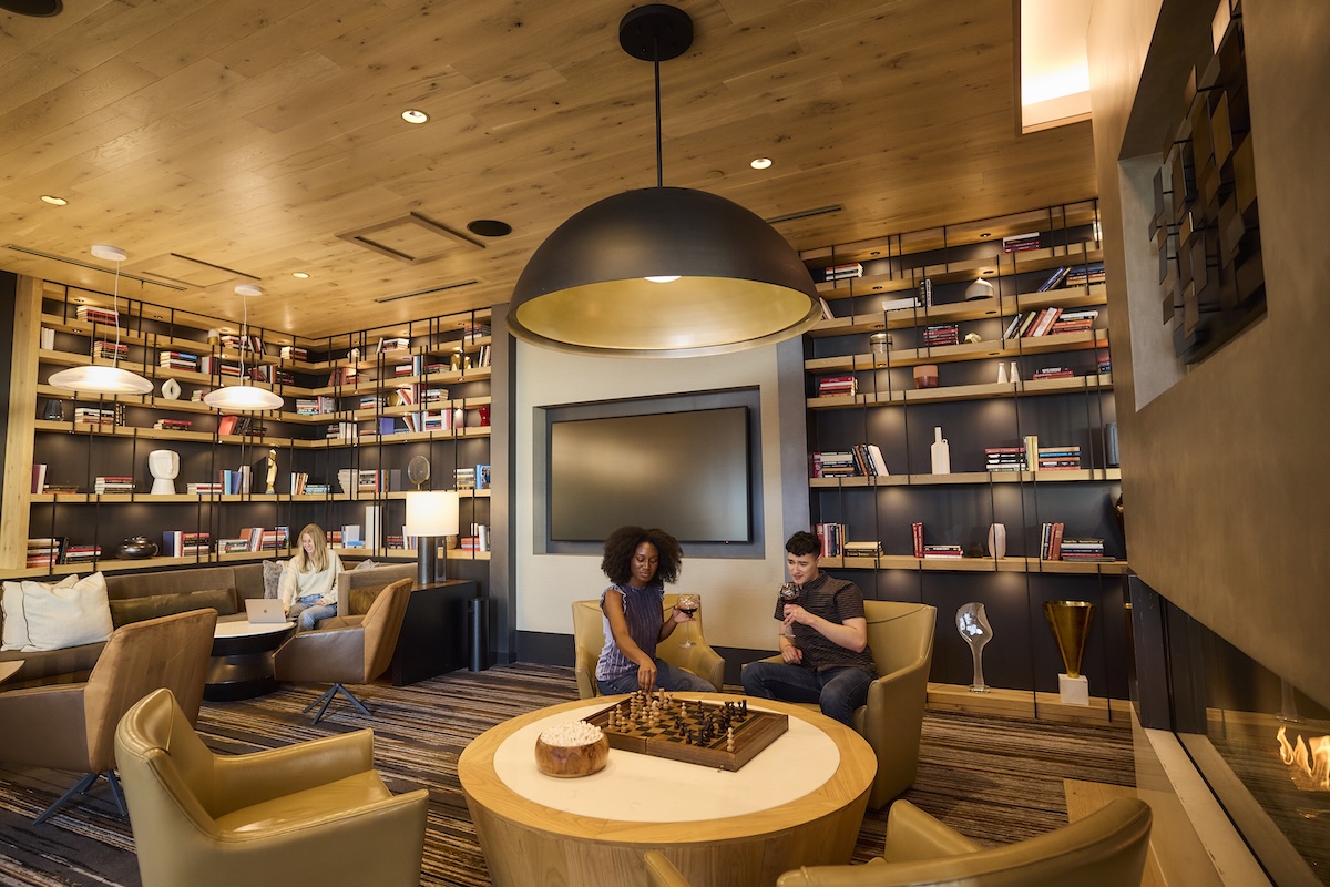 Residents playing chess in a lounge with built-in bookshelves and fireplace at One Cardinal Way