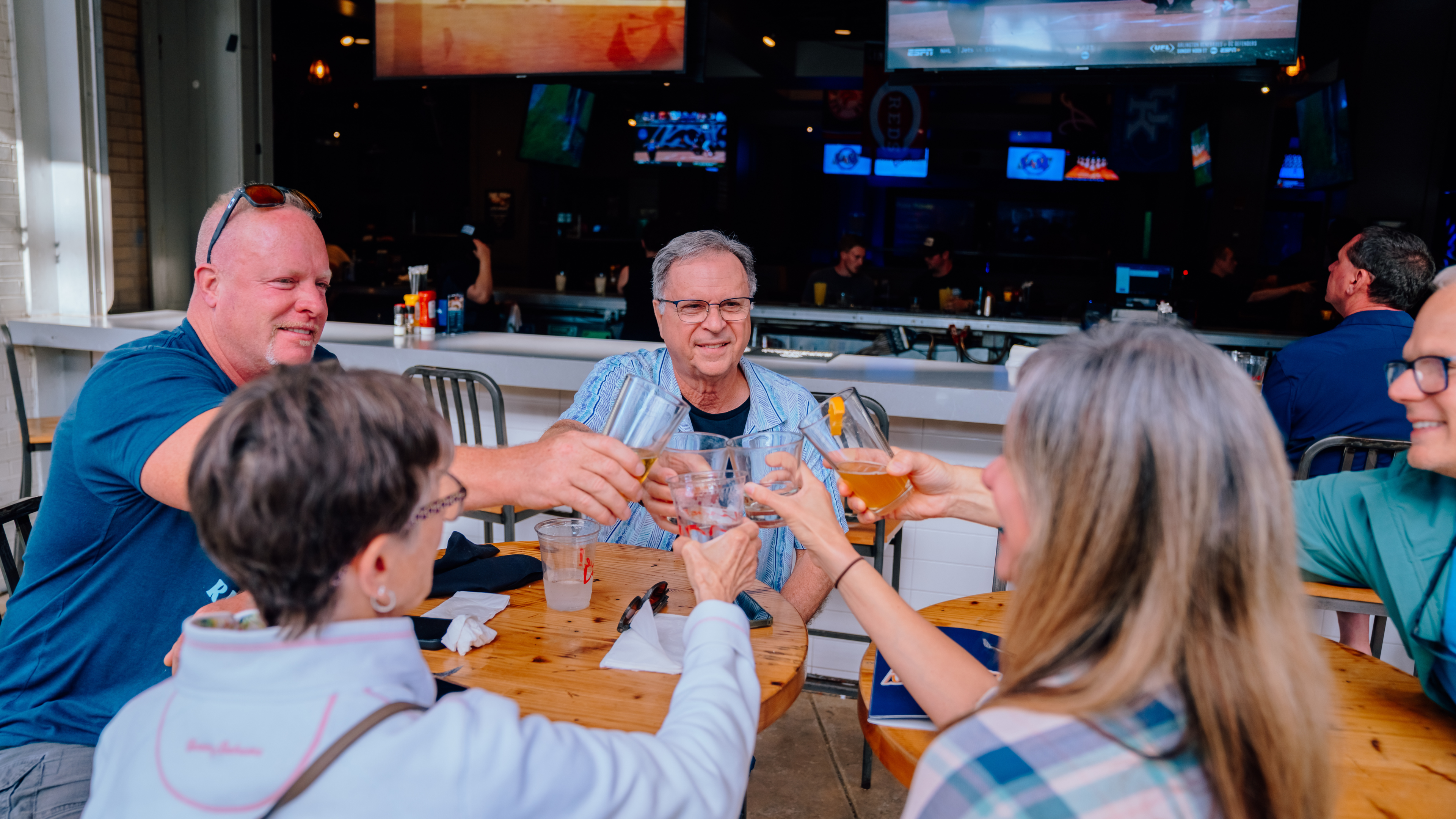 A group of people clinking their drinks together on the Sports and Social patio.