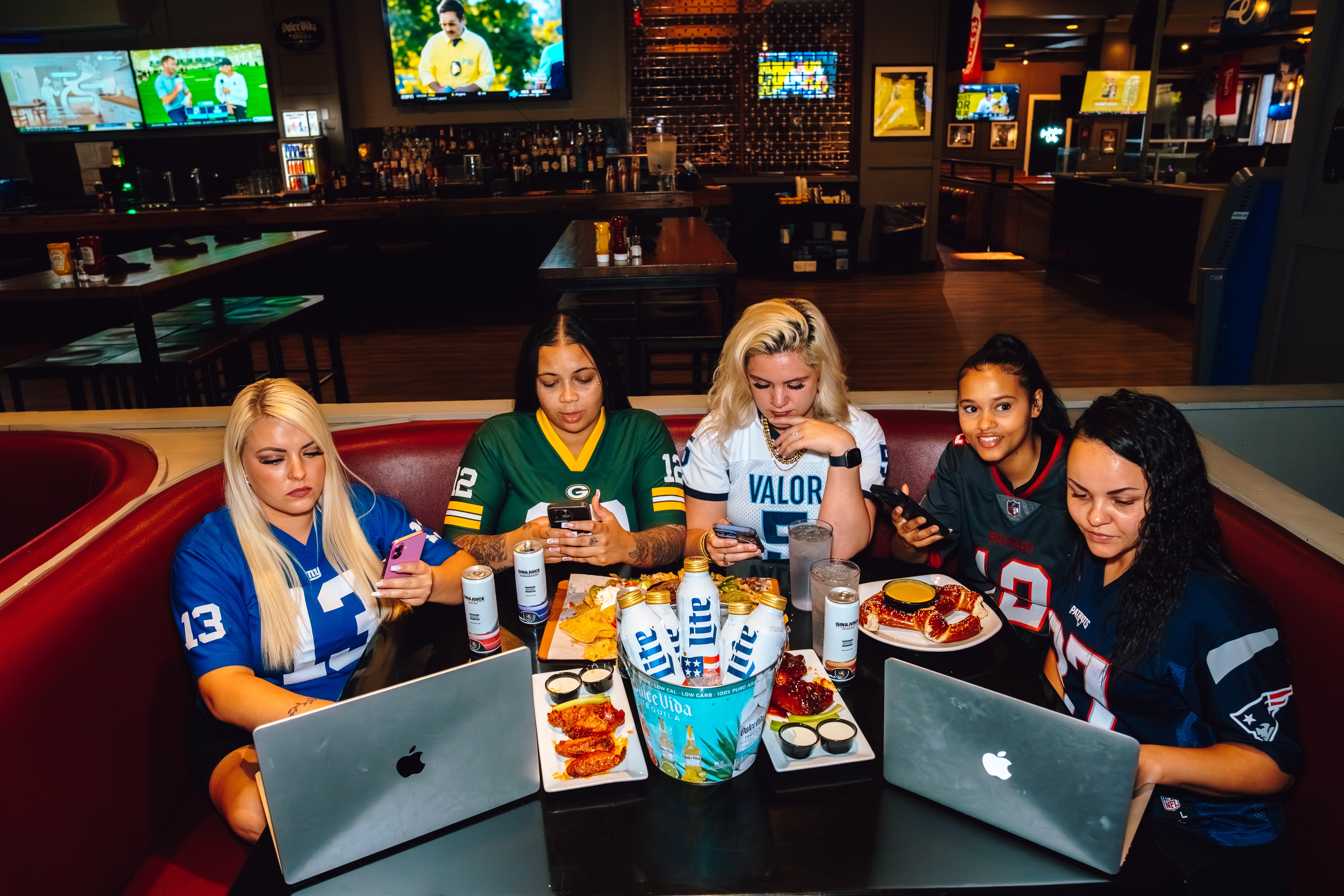 An image of 5 ladies wearing football Jerseys sitting in a booth.