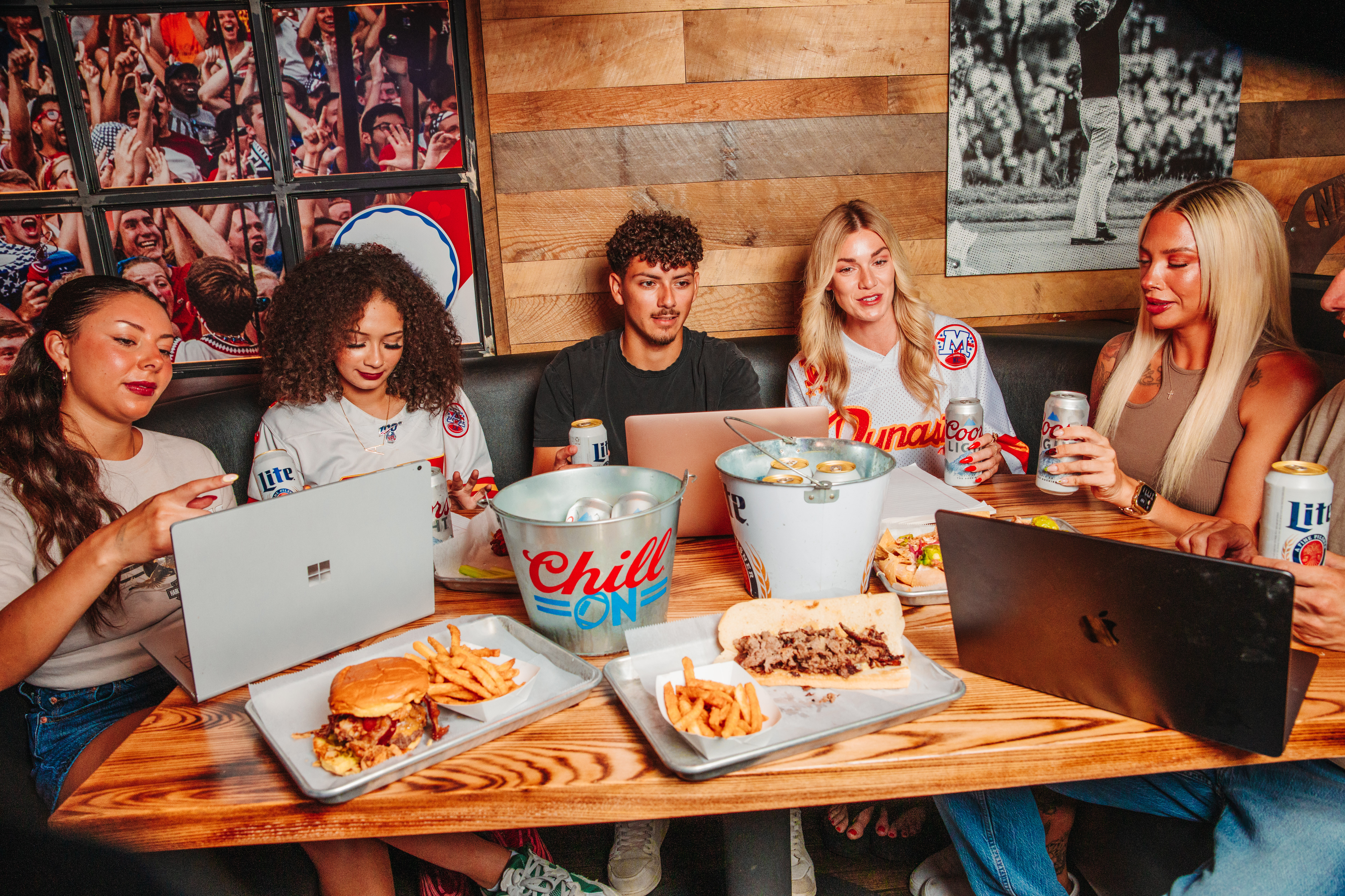 An image of guys and girls sitting at a booth with food ad laptops on the table.