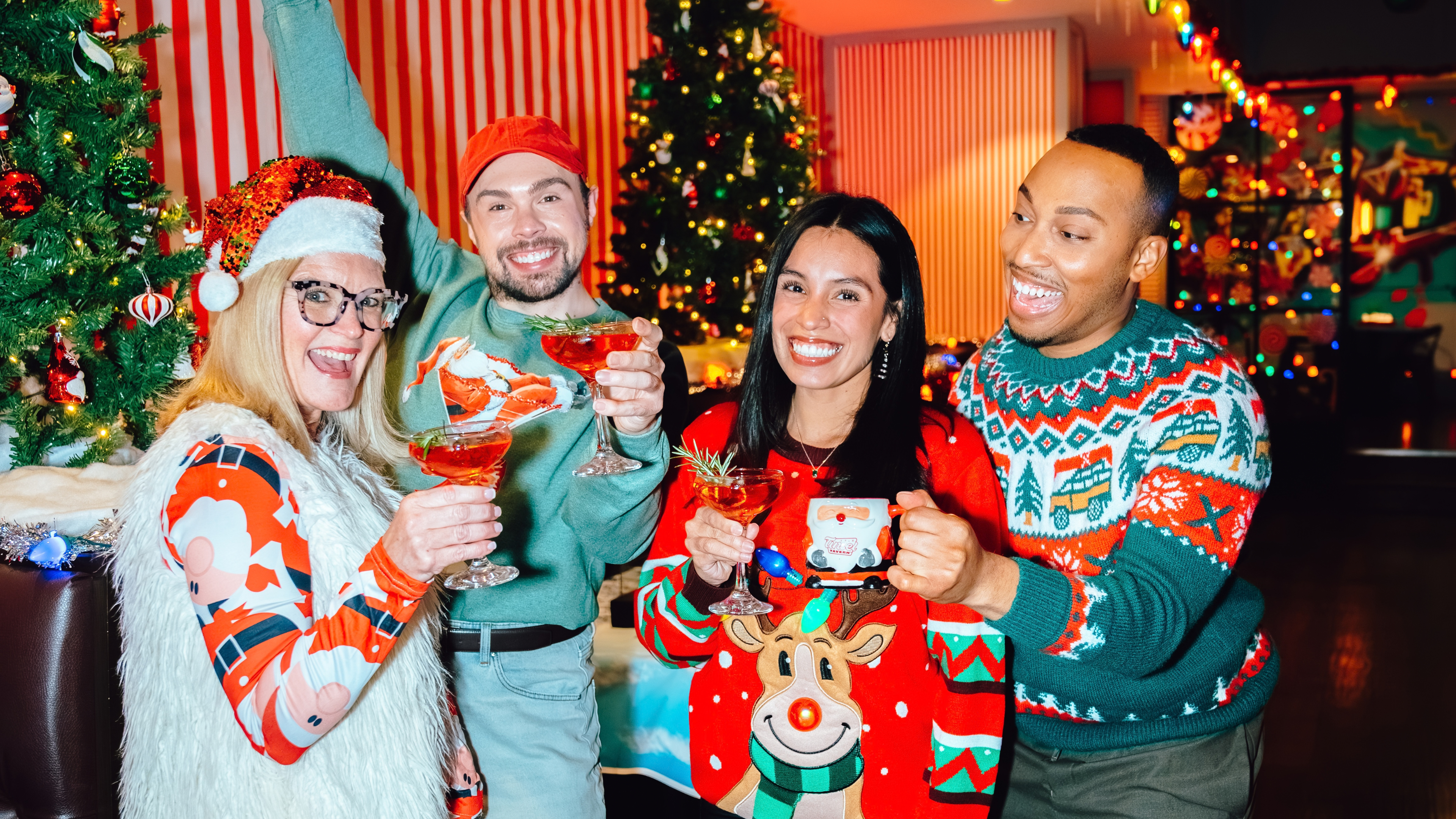 An image of two women and two men cheering their holiday drinks at tinsel Tavern, with one man throwing one arm up and the holiday decor behind them.