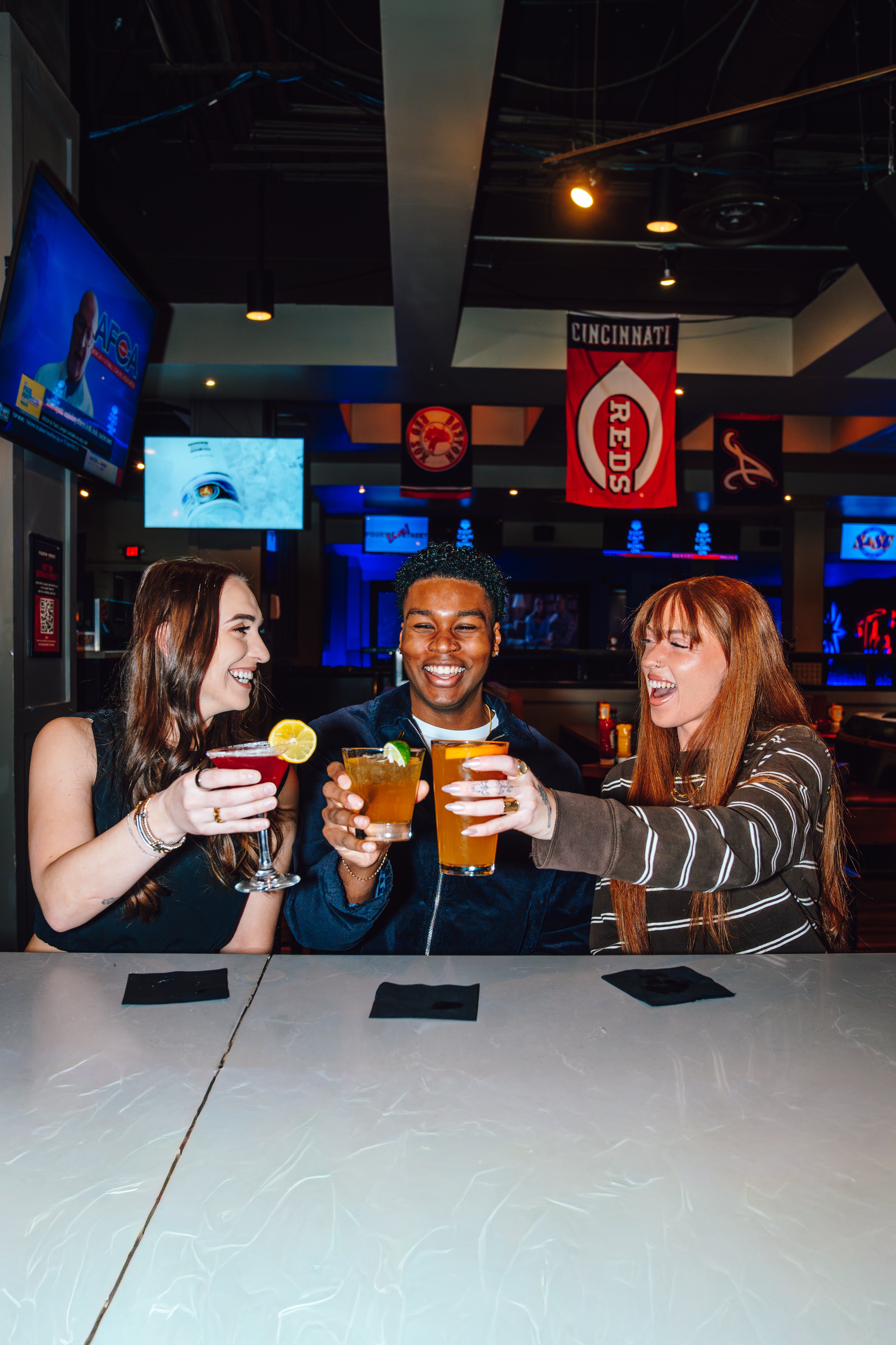 An image of two girls and a guy cheering their drink at the bar.
