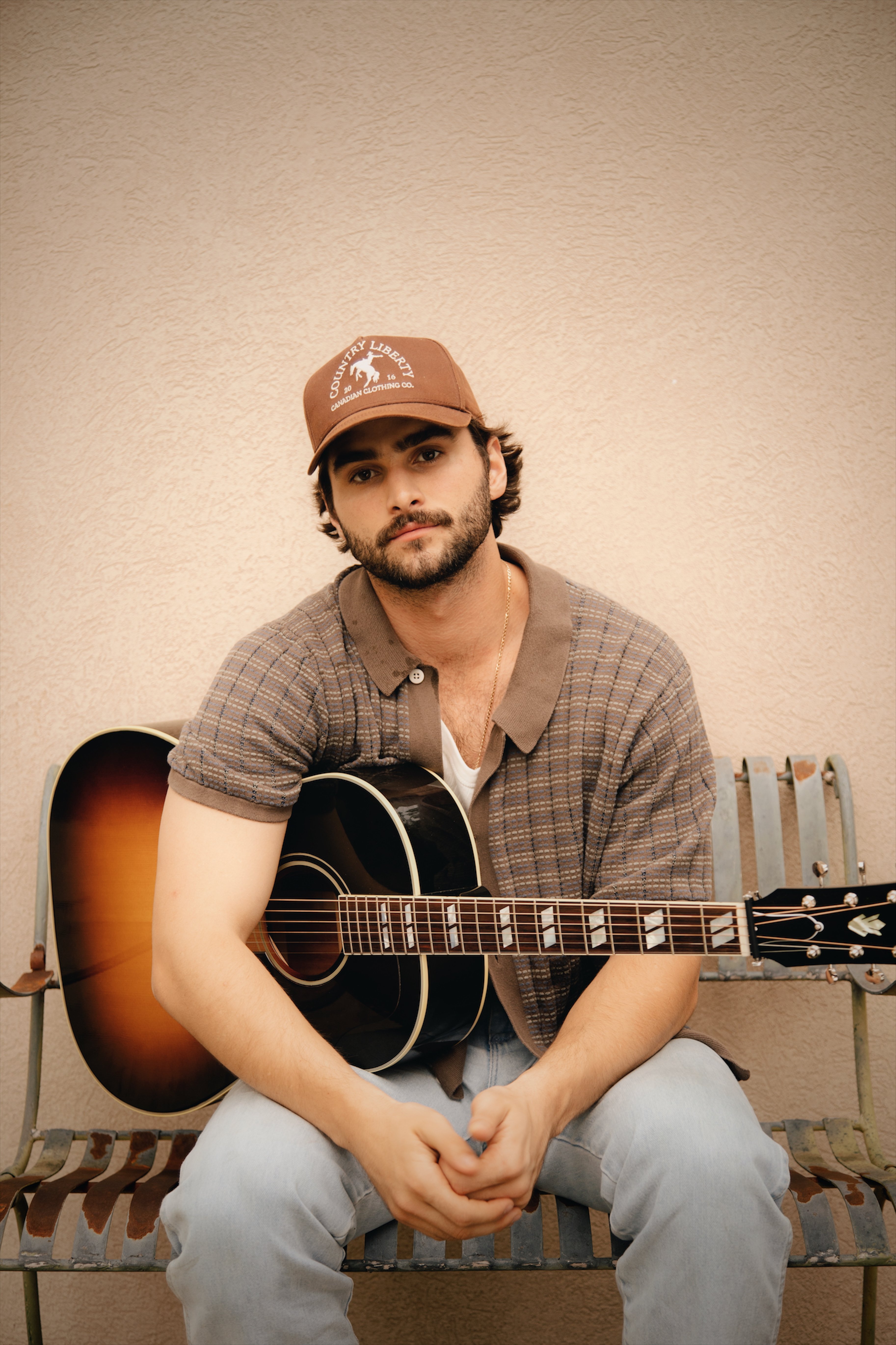 An image of Brendan Walter posing and sitting down with his guitar on his lap.
