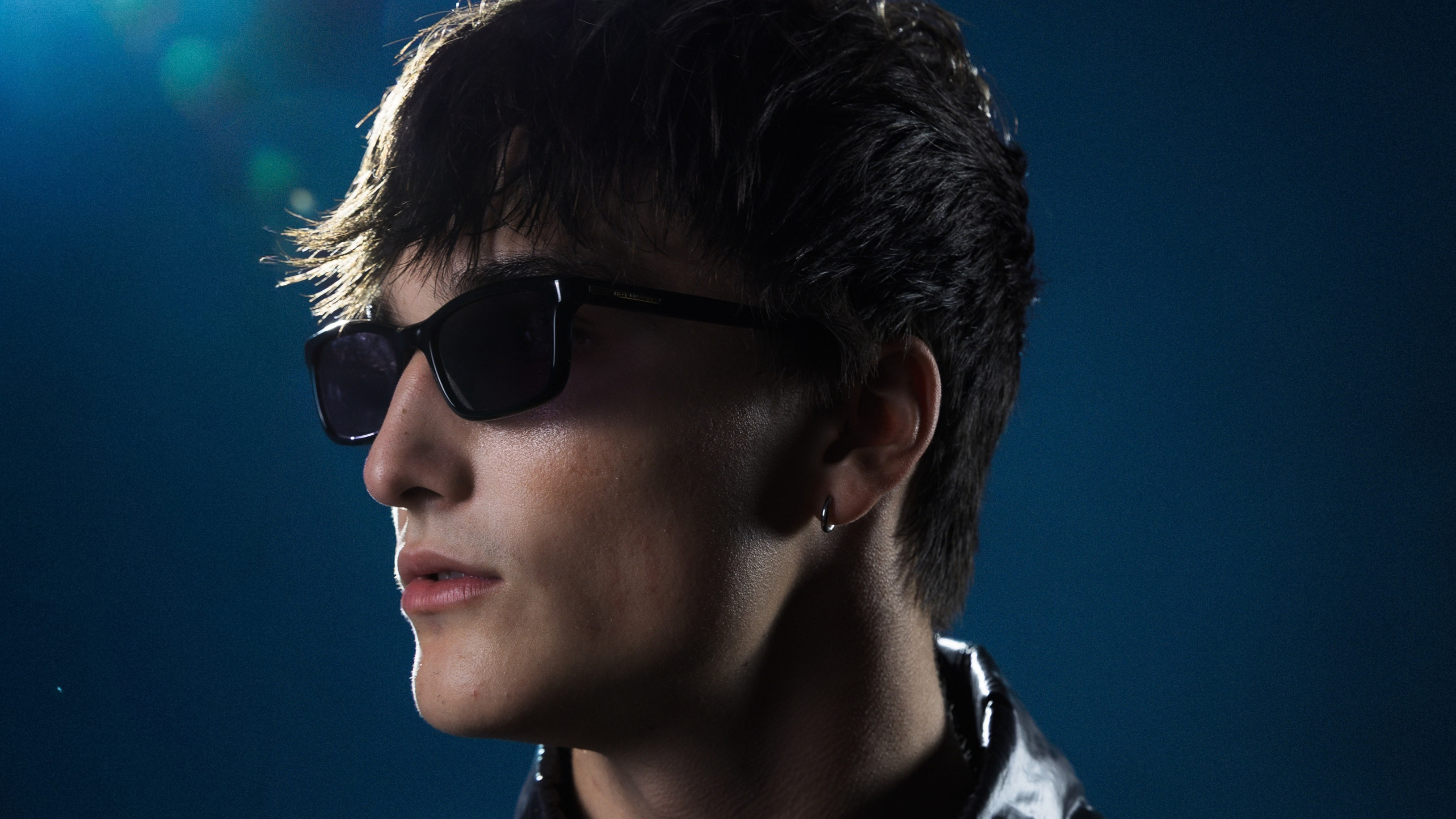An image of GudGroove wearing sunglasses and looking to the left, with a b lea background.