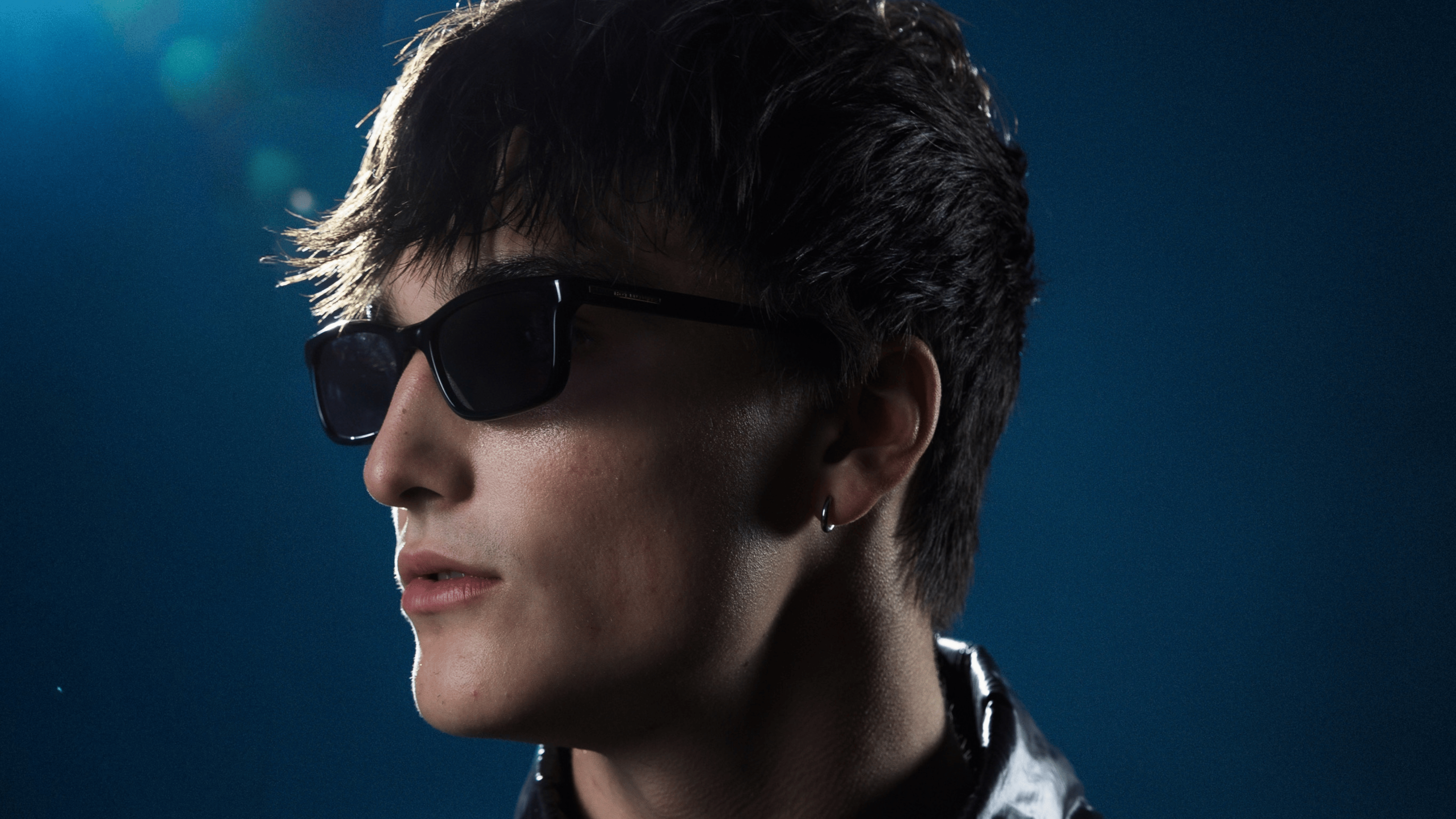 An image of GudGroove wearing sunglasses and looking to the left, with a b lea background.