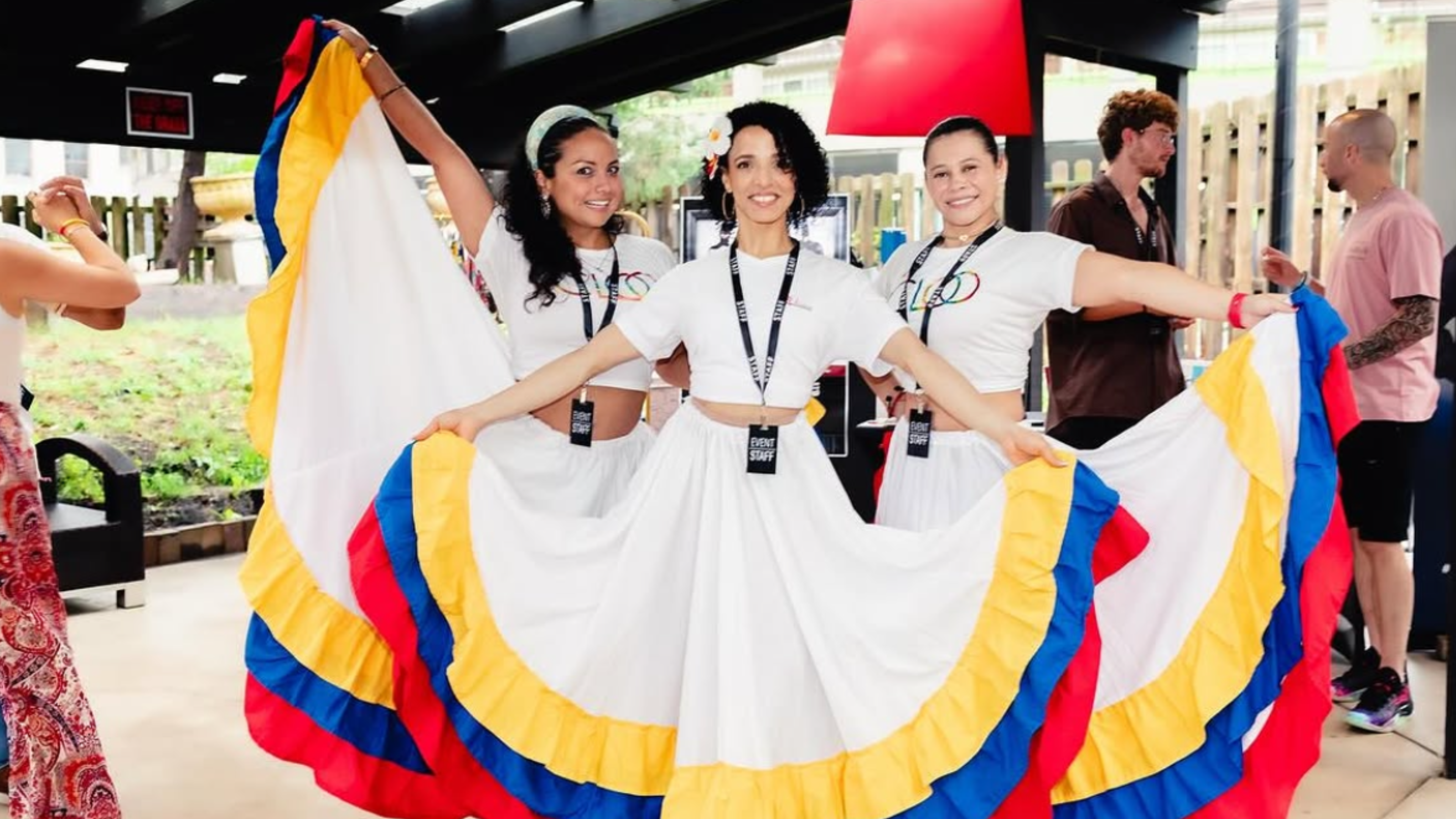 An image of 3 dancers wearing dresses with the Colombia flag colors, red, blue, and yellow.