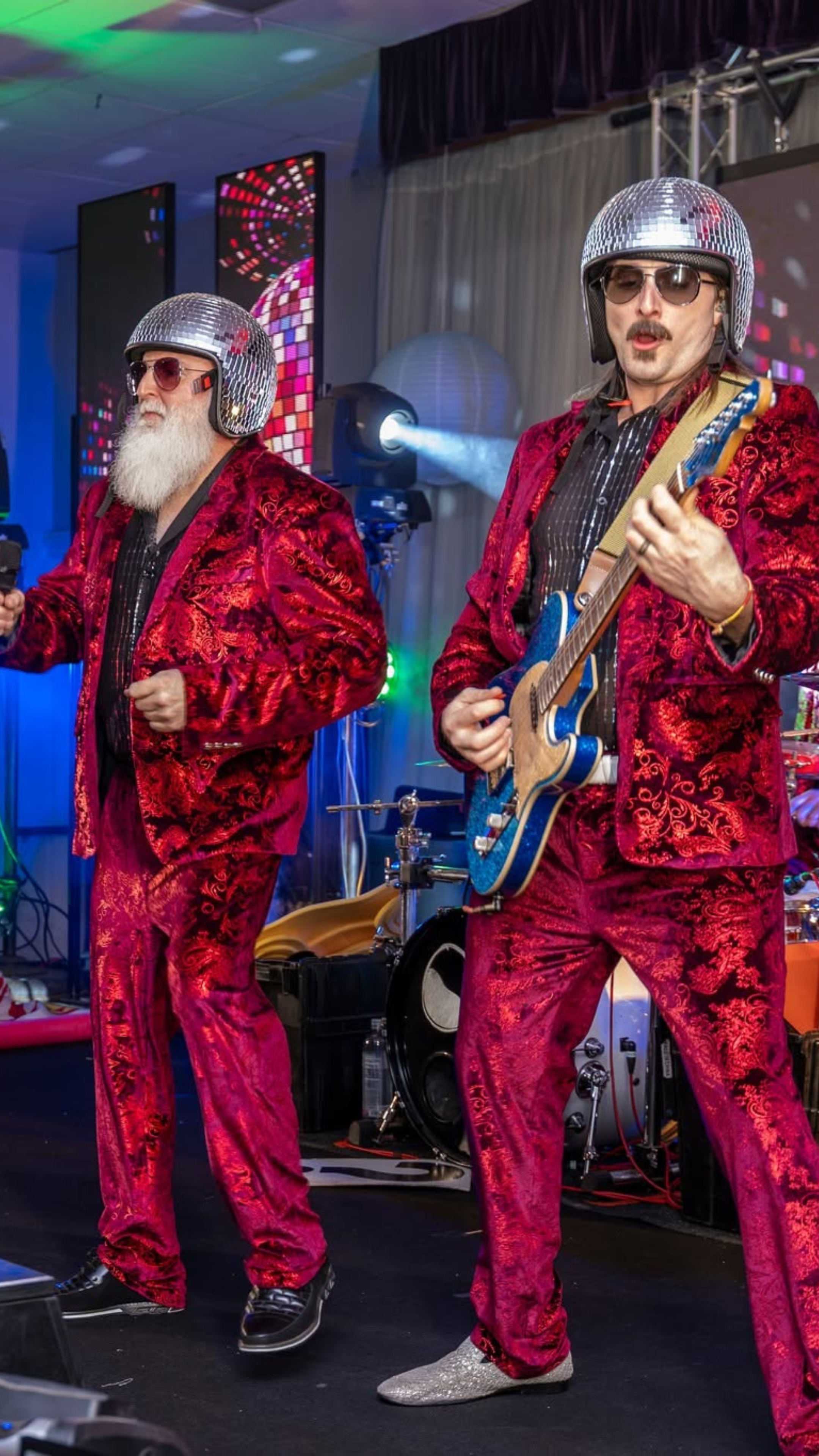 An image of two male members of the karate Girls Band performing, with one playing a blue guitar.