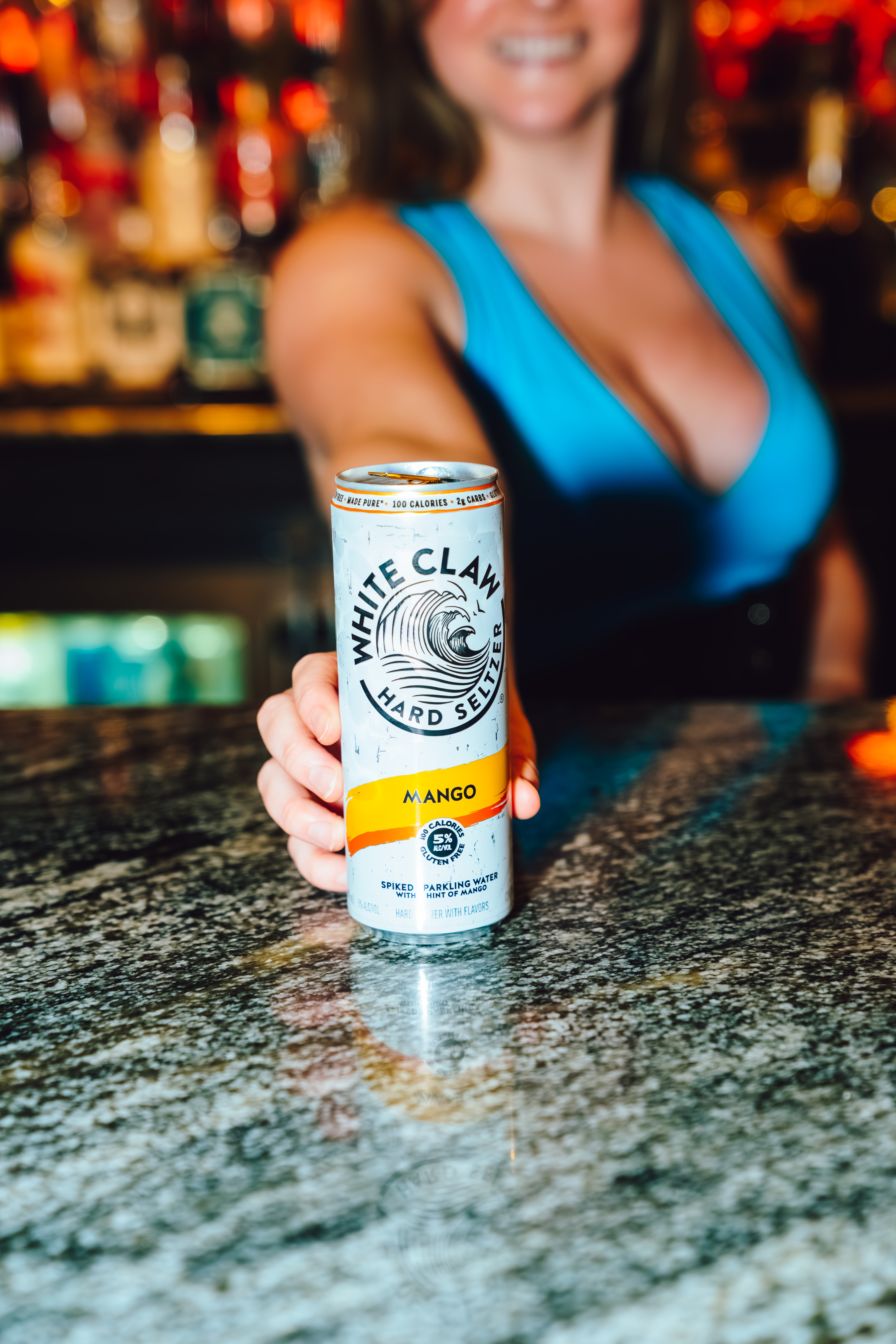 An image of a bartender holding out a can of White Claw on the bar.