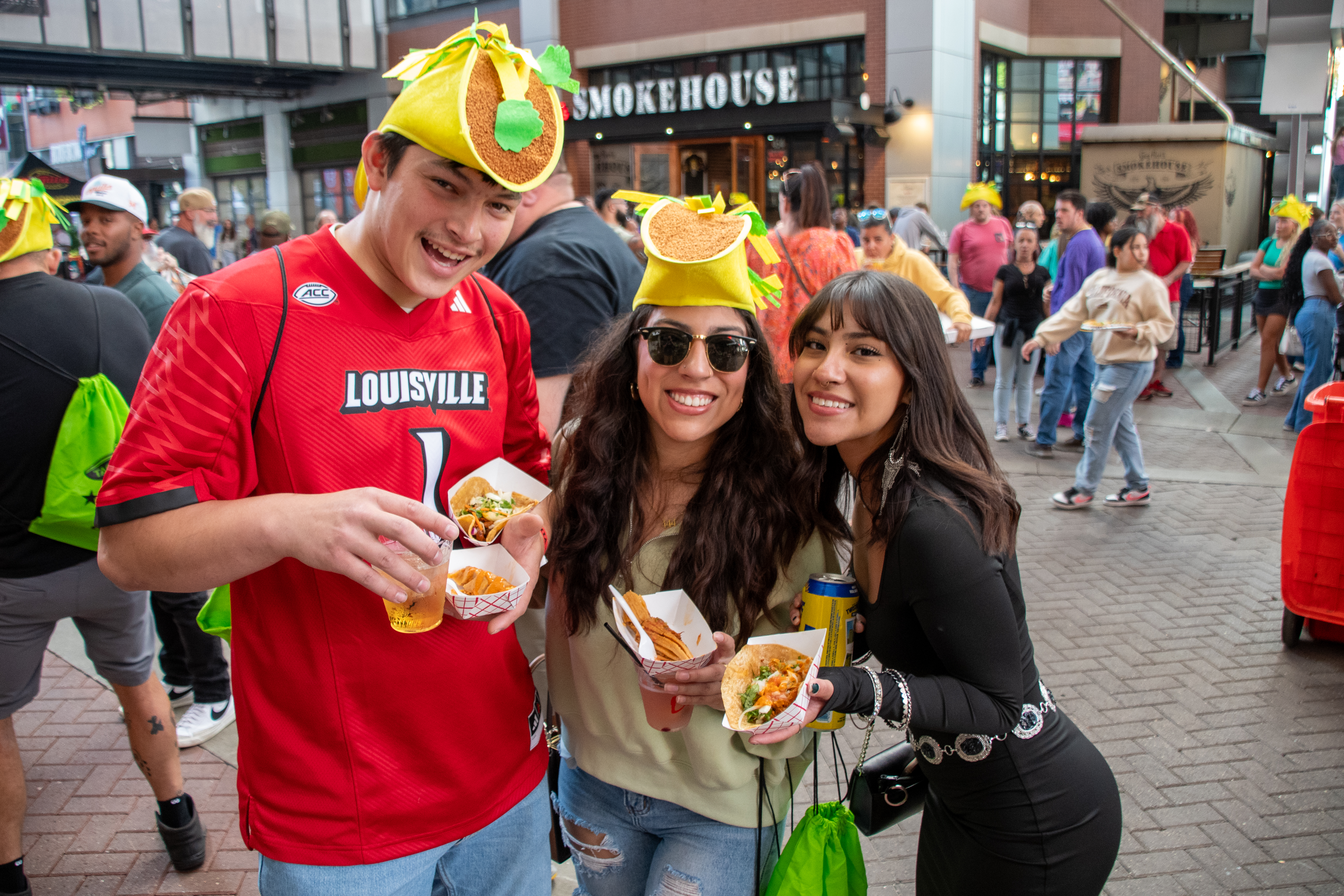 An image of a man and two women at taco fest wearing taco hats.