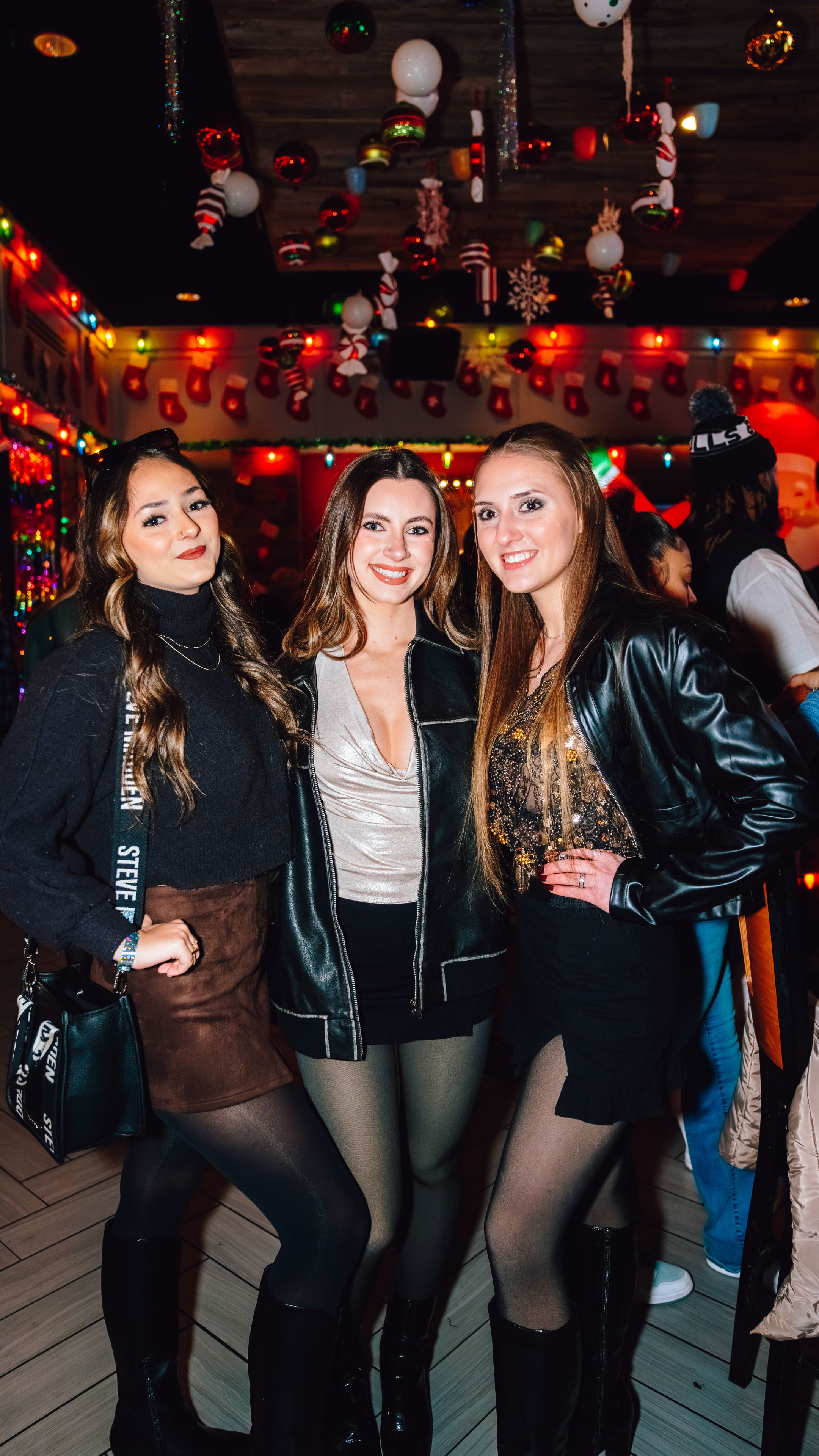 An image of three woman posing for a picture together at the Holiday bar, Tinsel Tavern, and all wearing skirts and black clothing.