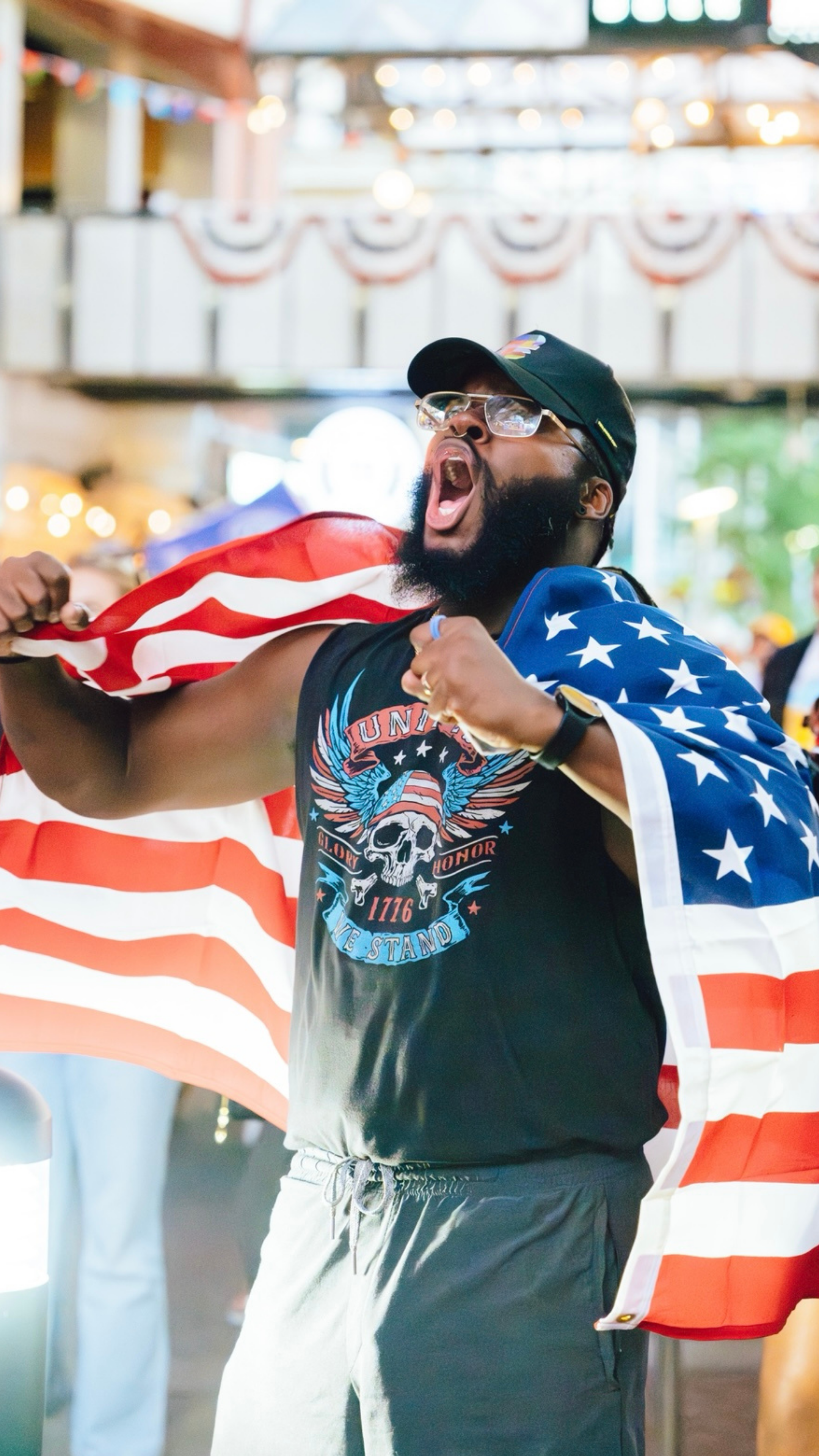 An image of a guy cheering for USA and wearing an American flag on his back.