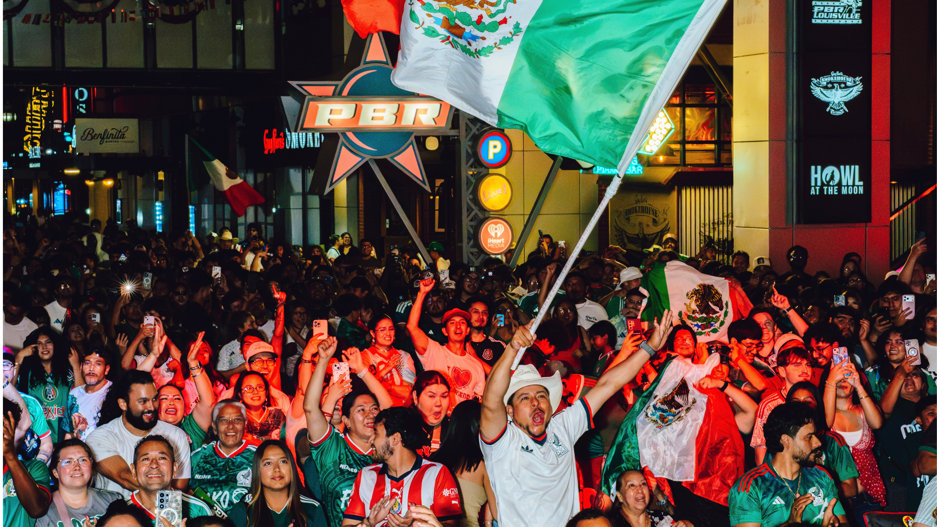 An image of Mexico fans all cheering and one person holding up a Mexico flag.
