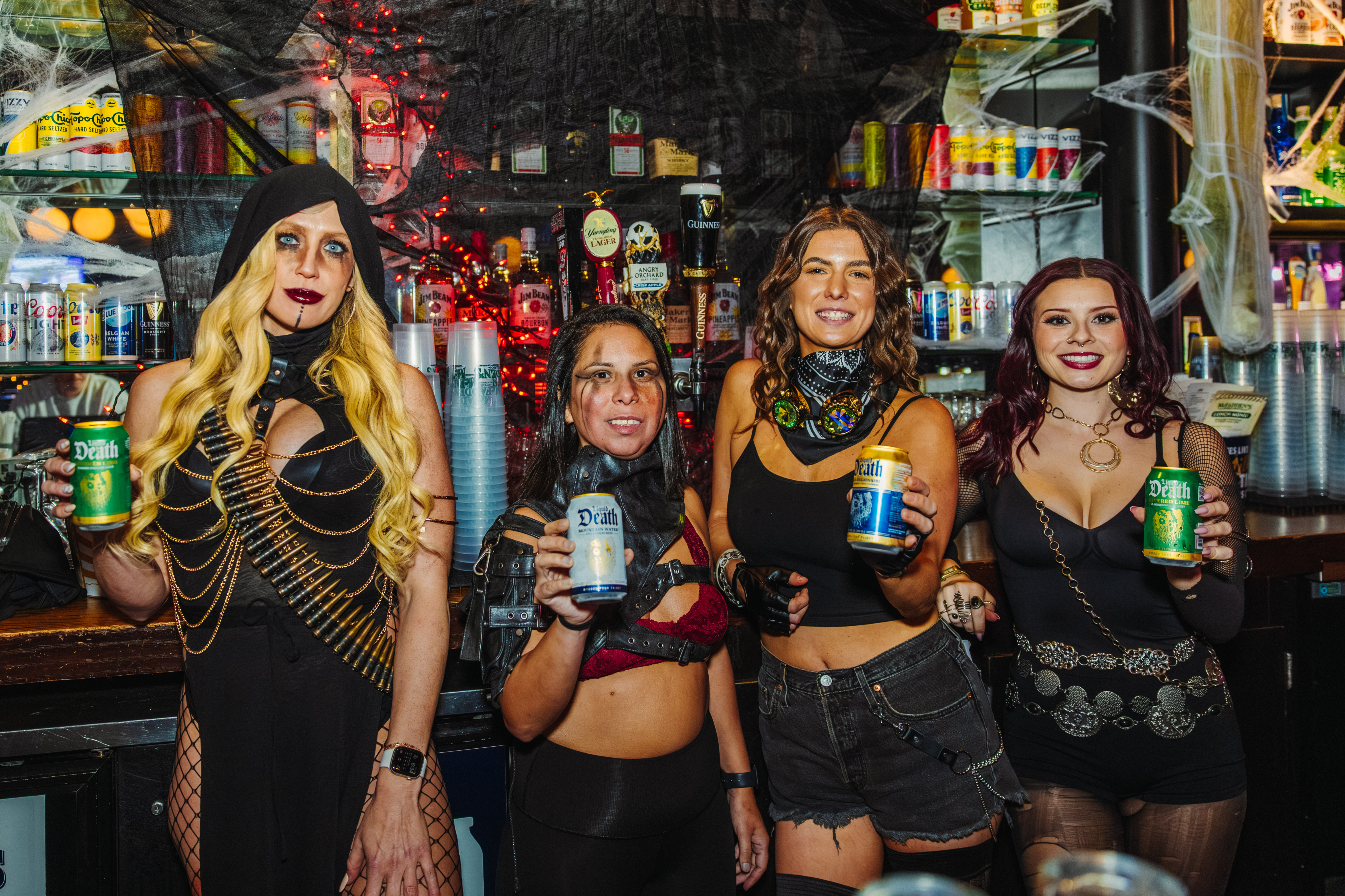 Four bartenders in Halloween costumes holding drink cans
