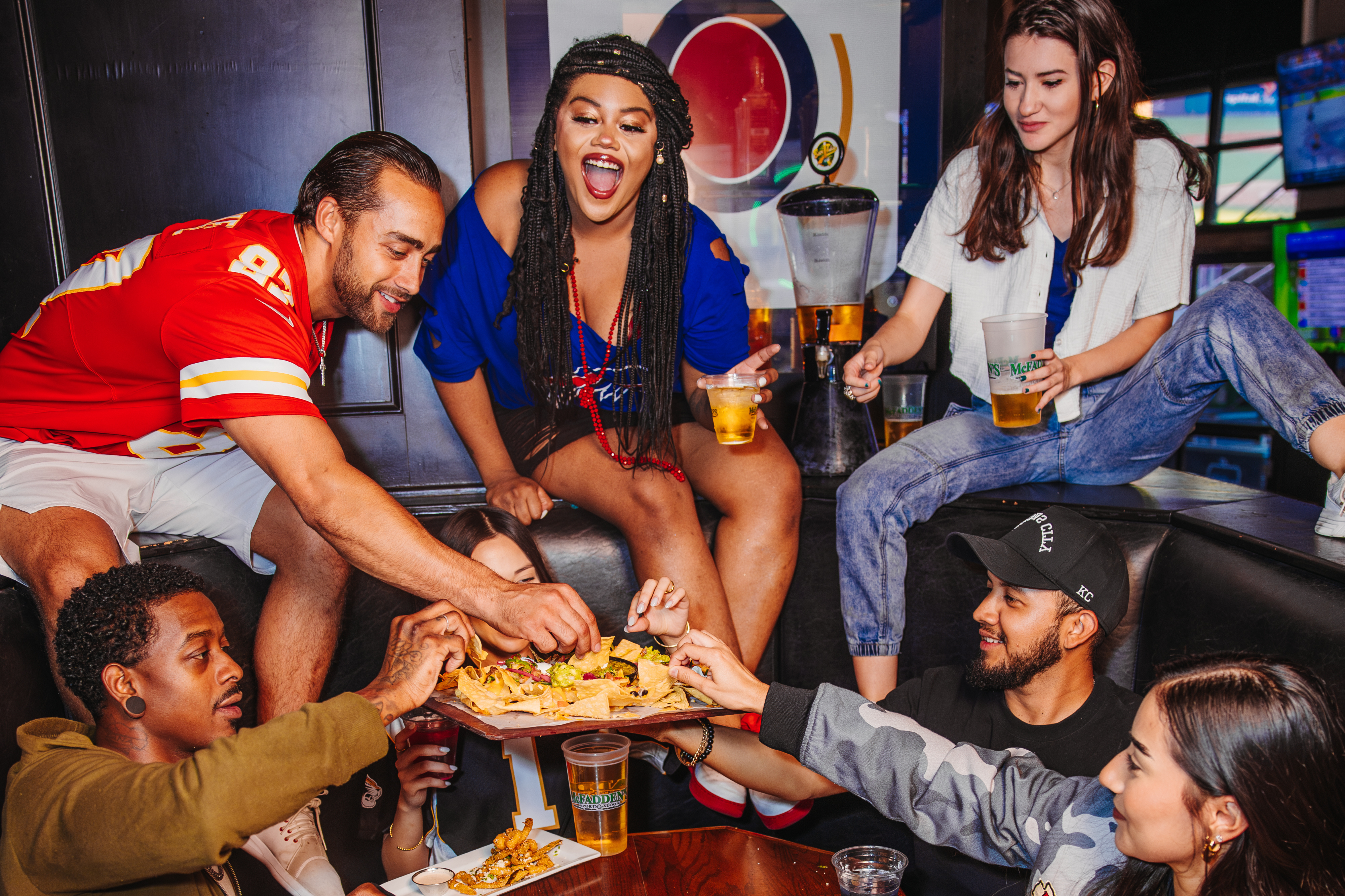 Group of friends sitting in a booth eating a plate of nachos 