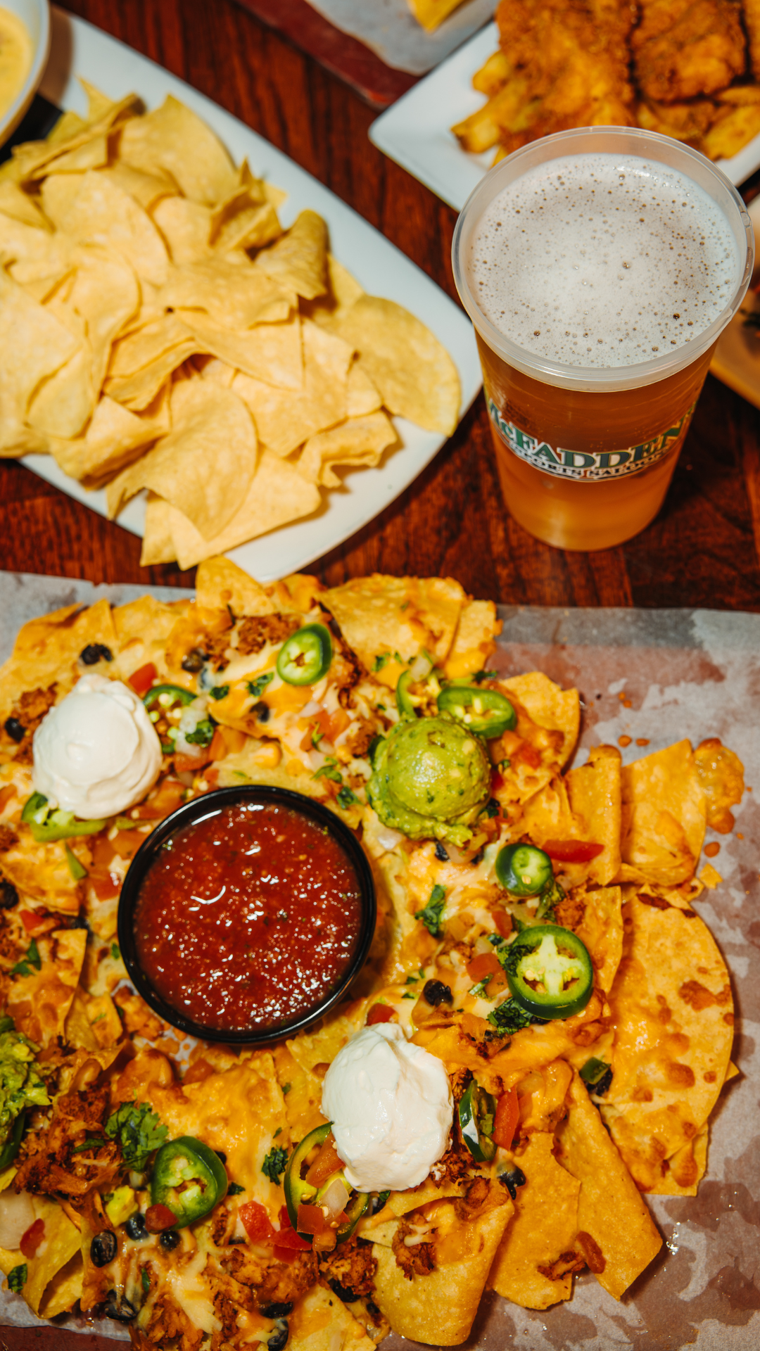 Plate of nachos, plate of chips, and pint of beer on a table