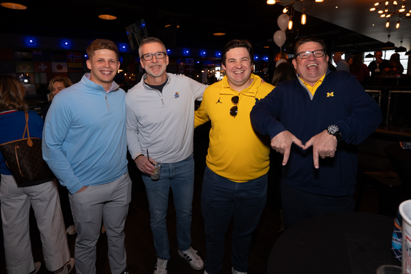 Four men in various college sports merchandise standing at No Other Pub